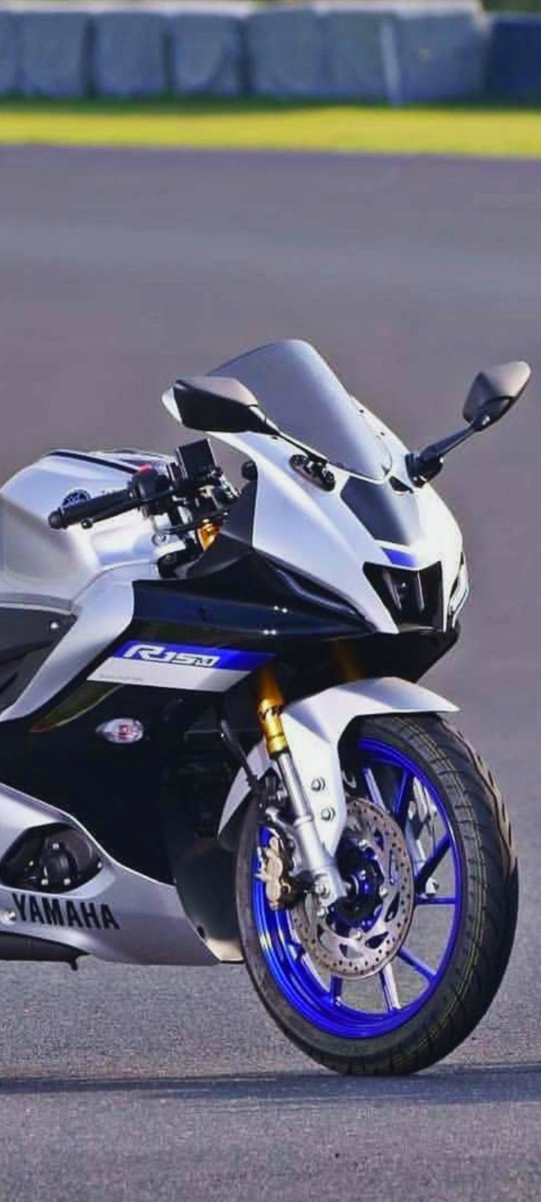 桌布 壁紙 — 一輛銀藍色的Yamaha R15V3摩托車帥氣地停在瀝青賽道上，背景是模糊的綠化。