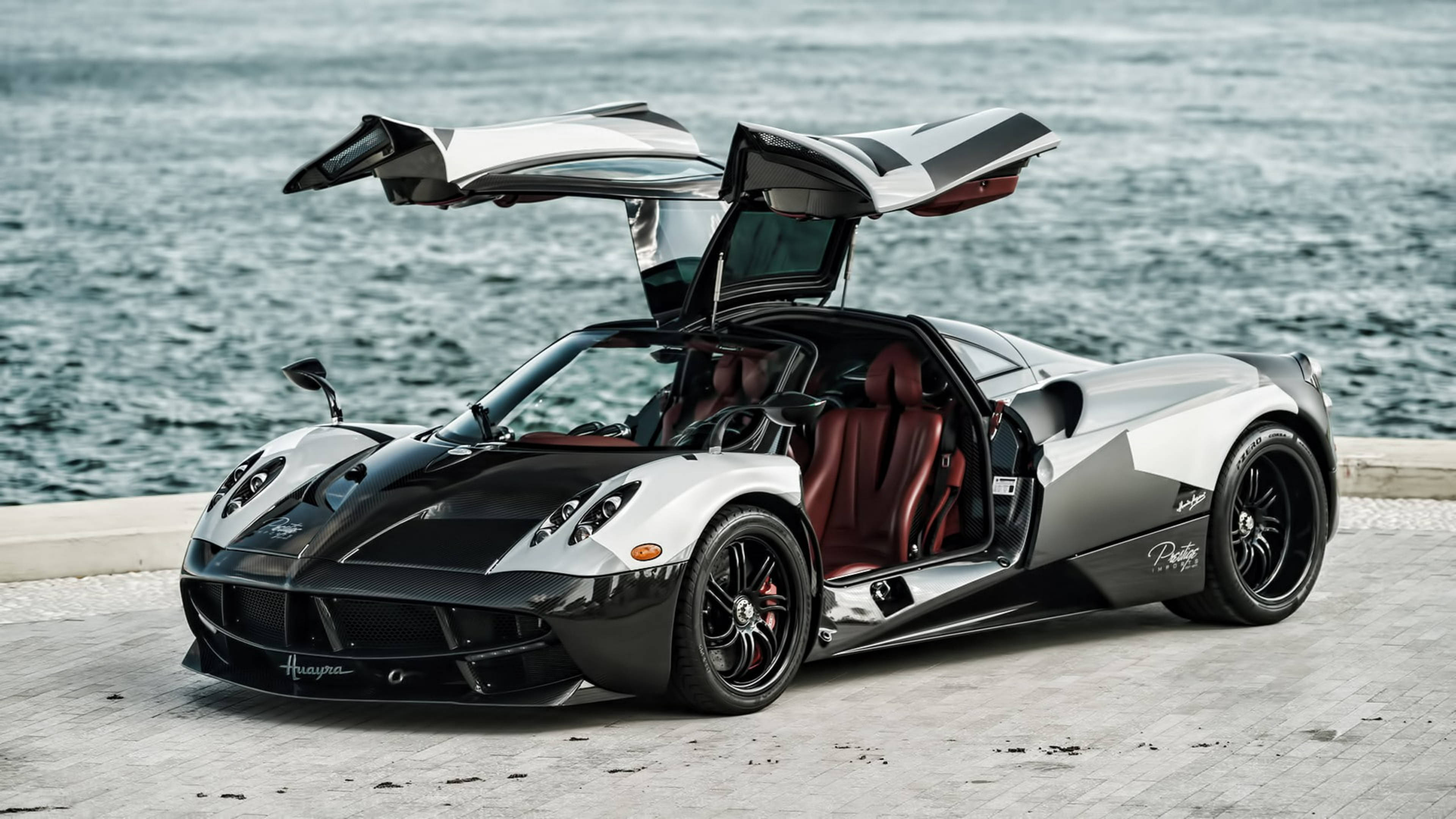帕加尼 桌布 壁紙 — 一輛銀黑配色的Pagani Huayra跑車，剪刀門打開，停在海濱碼頭上，俯瞰海洋。