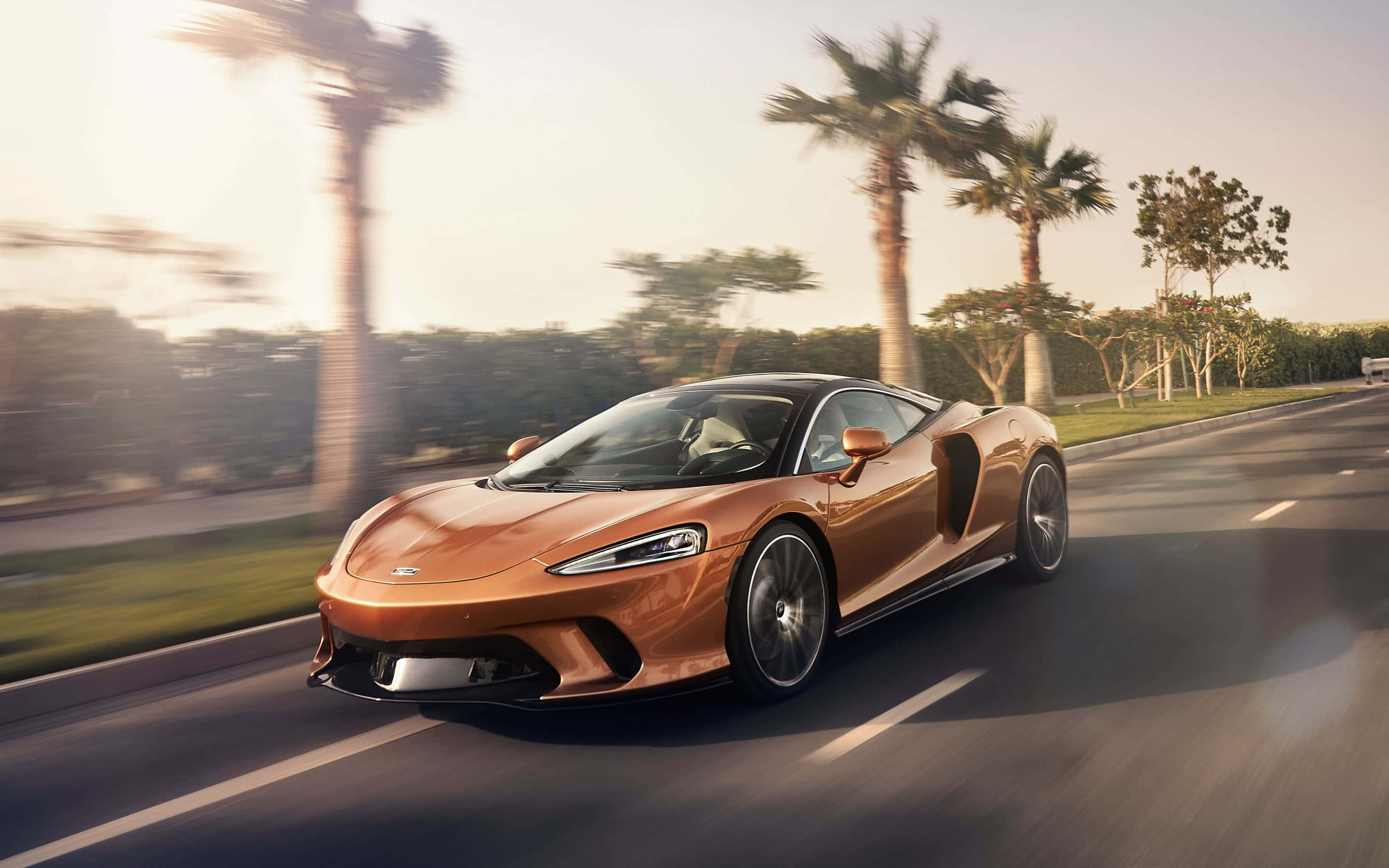 Bronze 桌布 壁紙 — 一輛銅色McLaren跑車在黃金時段沿著棕櫚樹成蔭的道路疾馳，動態模糊強調了速度。