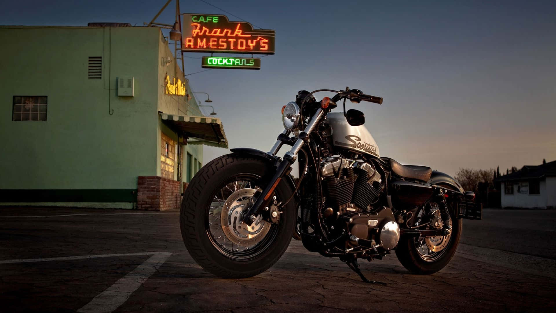 Harley Davidson HD 桌布 壁紙 — 一輛鍍鉻摩托車在黃昏時停在一間霓虹燈咖啡館前，周圍有溫暖的環境燈光。