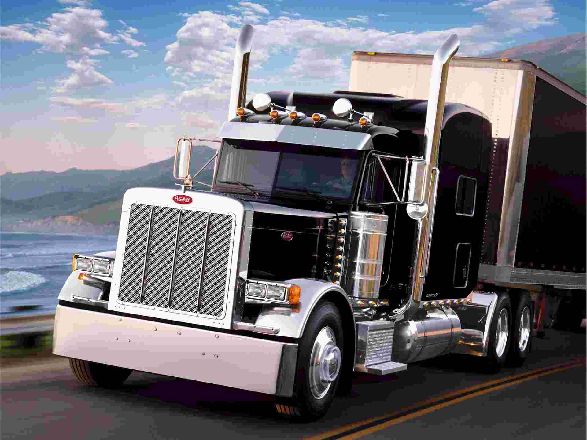 Peterbilt 桌布 壁紙 — 一輛閃亮的 Peterbilt 半掛卡車帶有鍍鉻裝飾，在部分多雲的天空下行駛在沿海高速公路上。