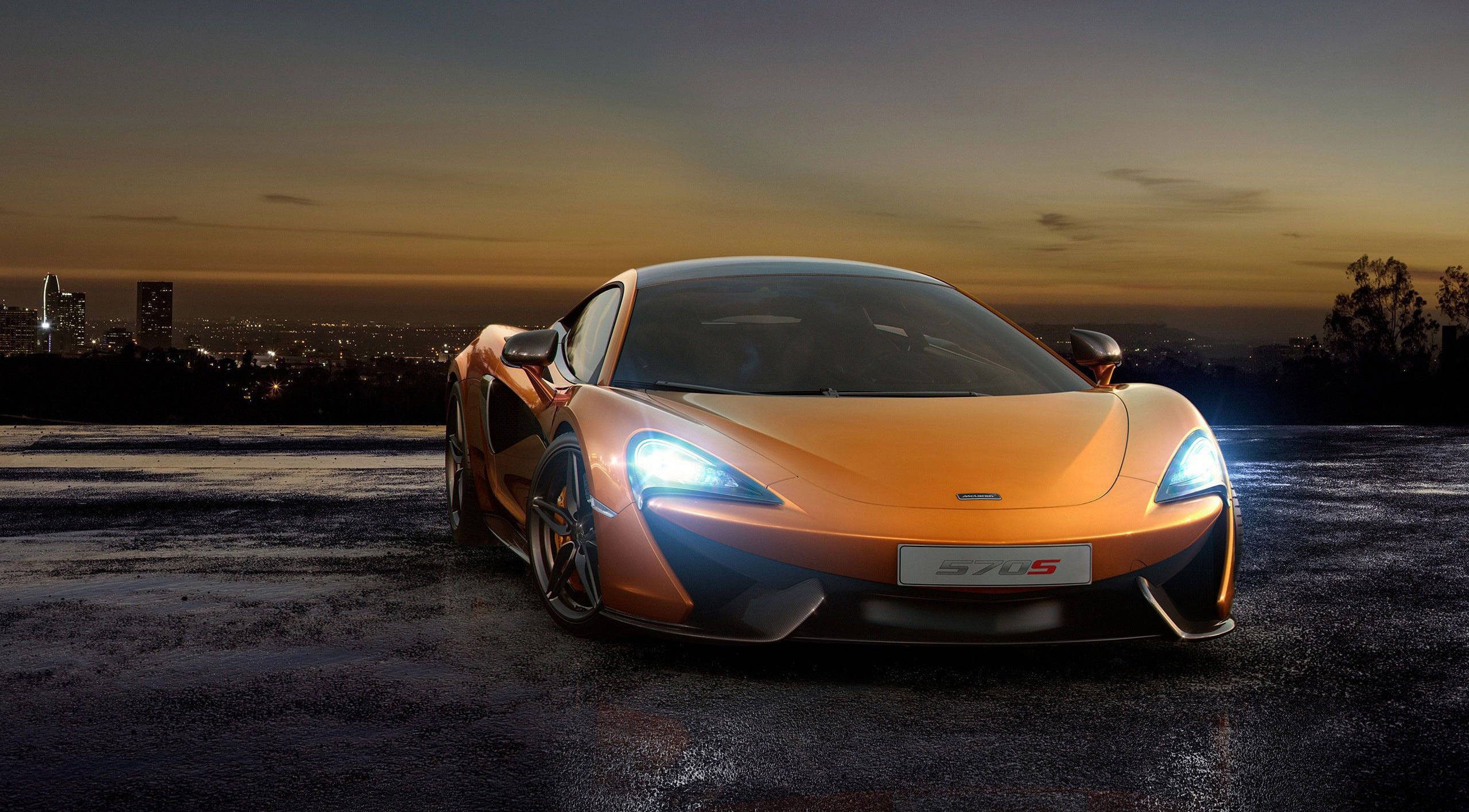 cars 桌布 壁紙 — 一輛閃亮的橙色McLaren 570S跑車，車頭燈發光，停在日落時分的濕漉漉屋頂上，俯瞰城市景觀。