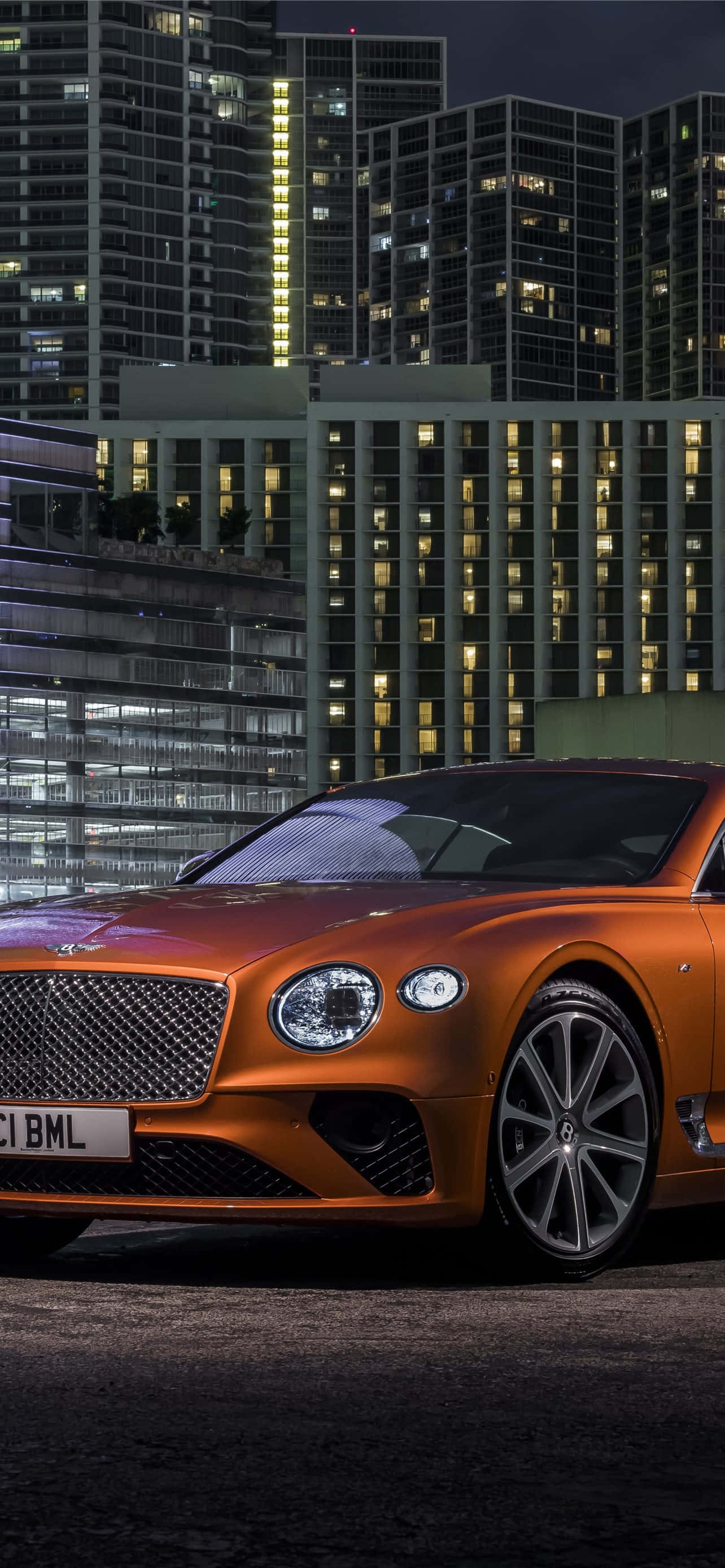 Bentley Continental Gt 桌布 壁紙 — 一輛閃亮的橙色賓利 Continental GT 在夜晚停泊，背景是燈火通明的摩天大樓。