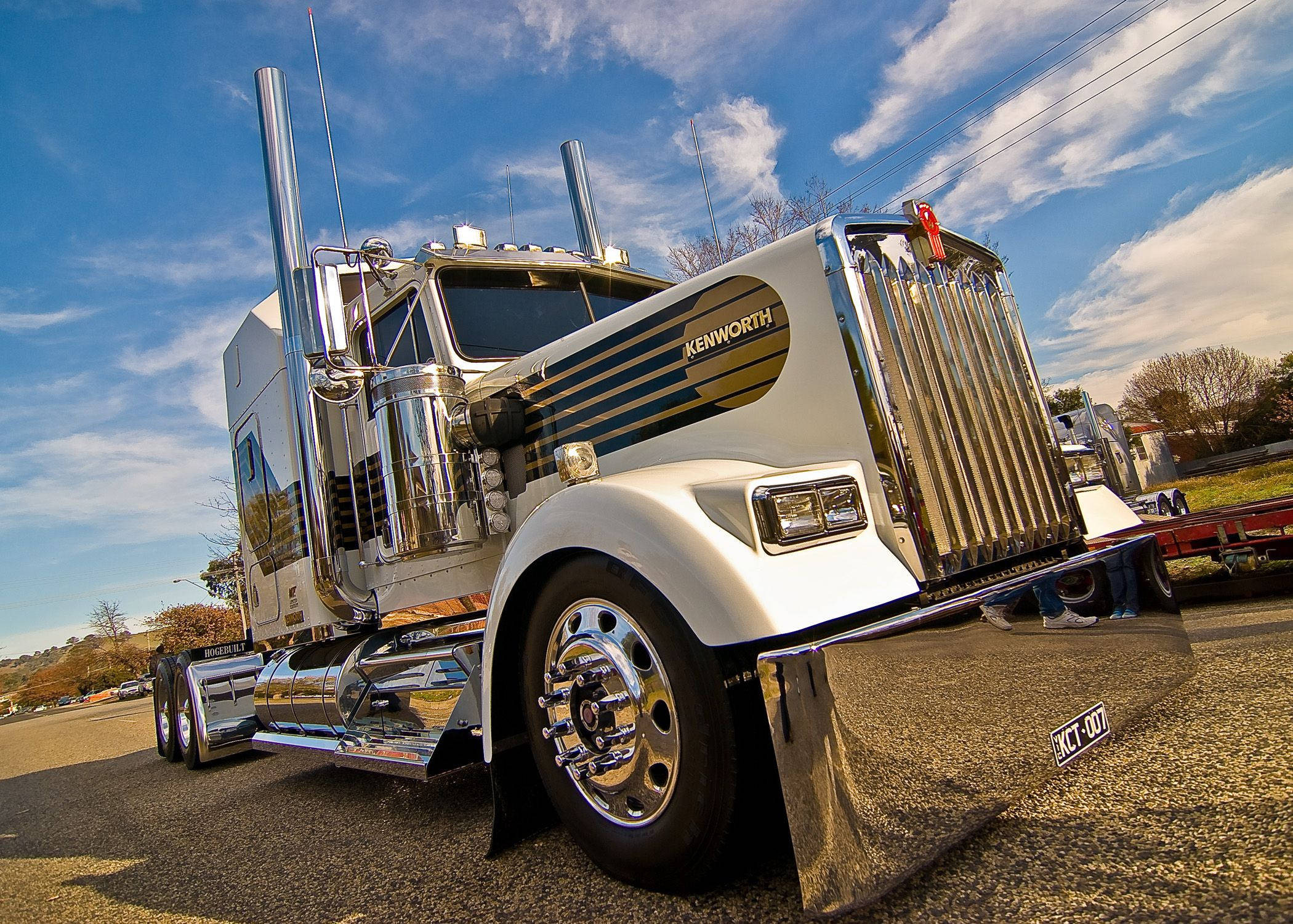 Kenworth 桌布 壁紙 — 一輛閃亮的白色Kenworth半掛卡車，帶有鍍鉻裝飾和高排氣管，停在藍天白雲下。