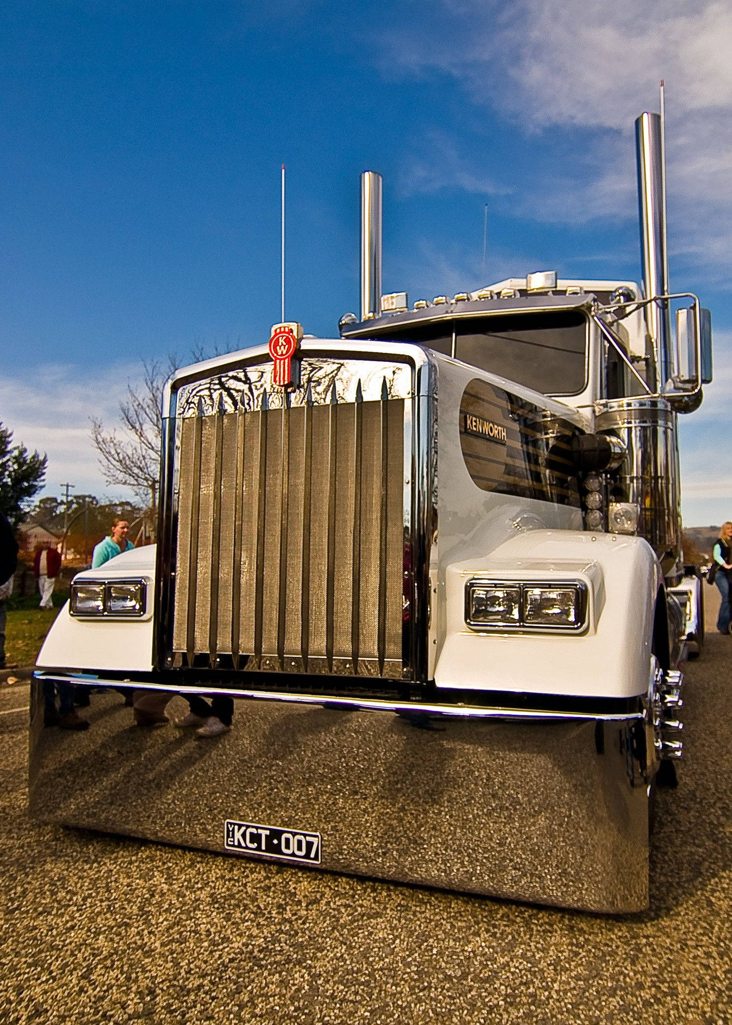 Kenworth 桌布 壁紙 — 一輛閃亮的白色Kenworth半掛卡車，帶有鍍鉻裝飾和雙排氣管，在晴朗的藍天下傲然矗立。
