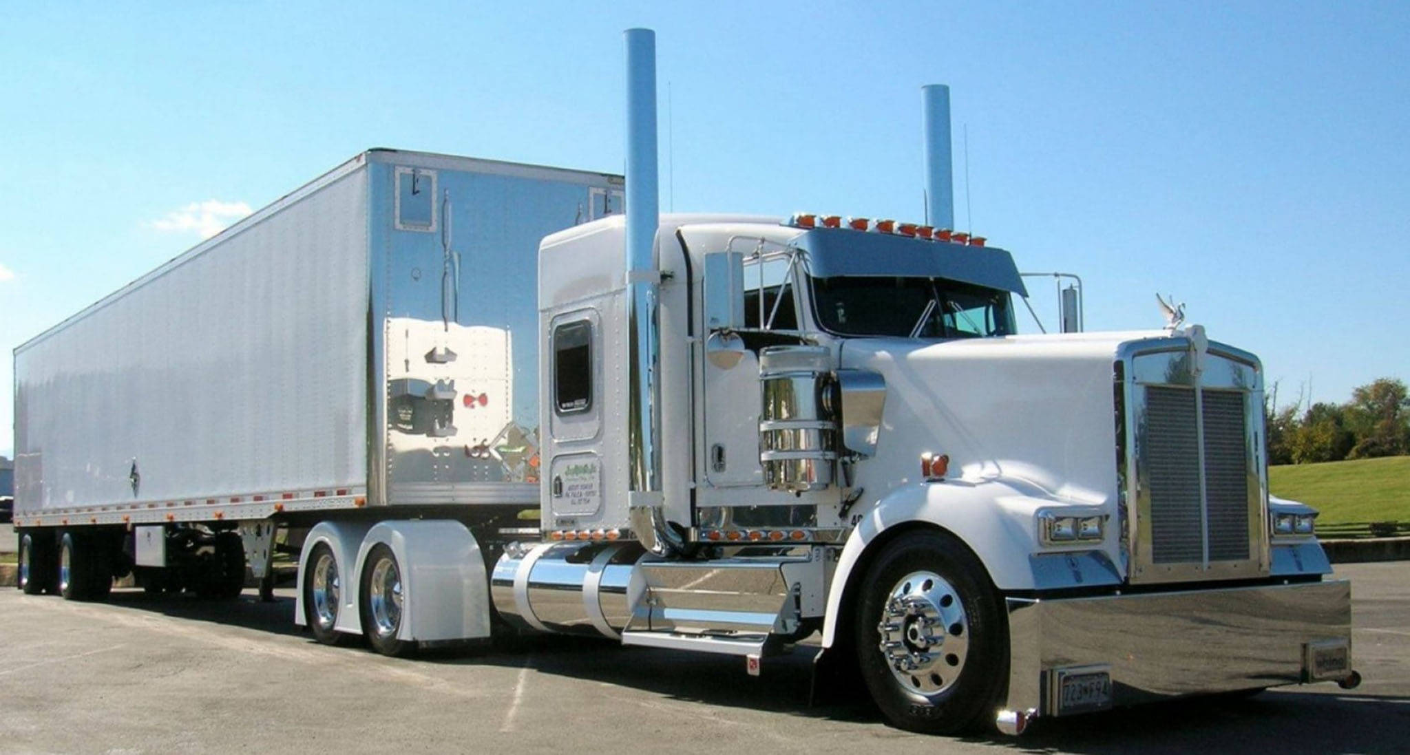 Kenworth W900 桌布 壁紙 — 一輛閃亮的白色半掛卡車，帶有鍍鉻裝飾和銀色拖車，停在瀝青路面上，背景是晴朗的藍天。