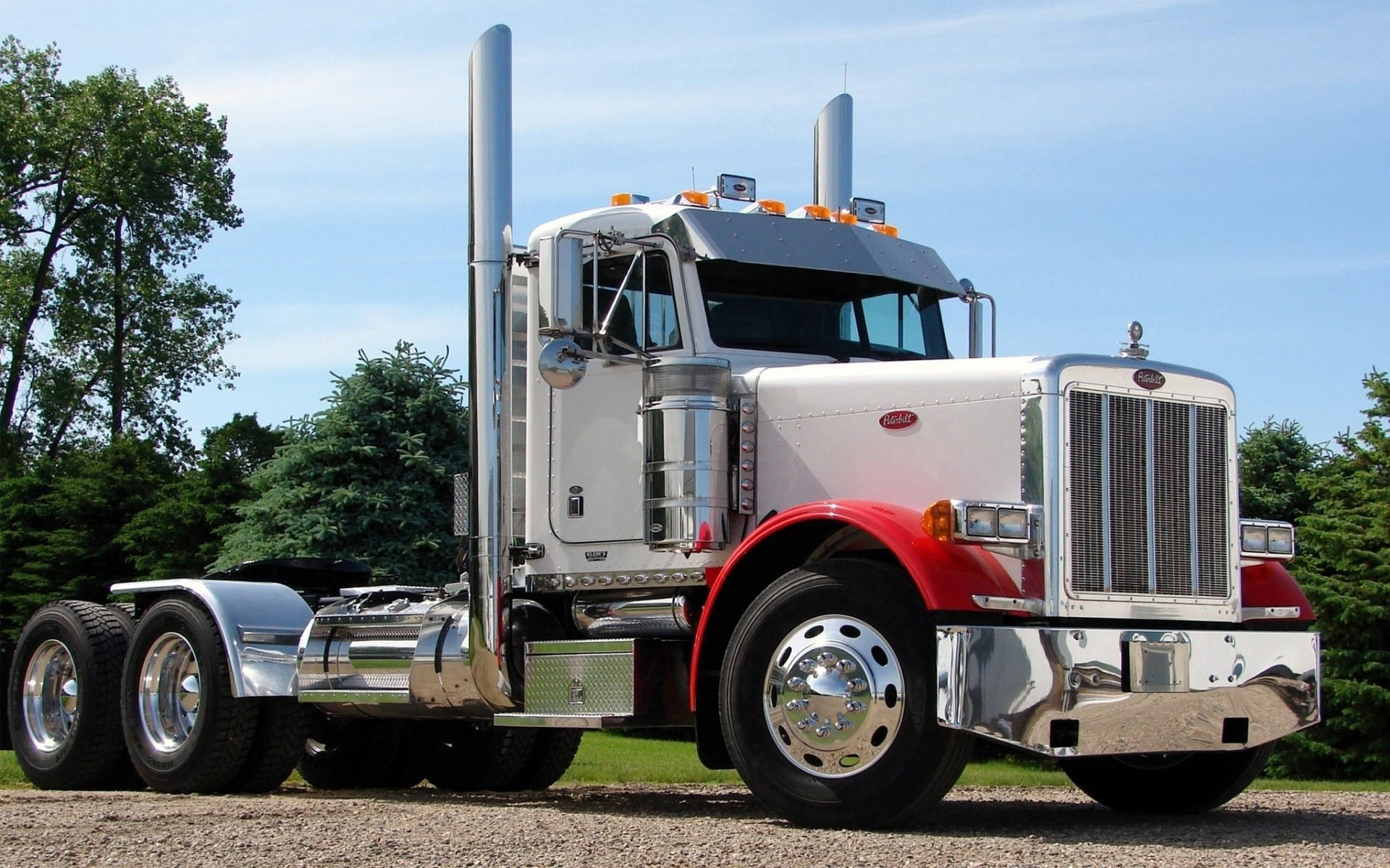 Peterbilt 桌布 壁紙 — 一輛閃亮的白色和紅色Peterbilt半掛卡車，帶有鍍鉻裝飾，自豪地停在碎石上，背景是晴朗的藍天。