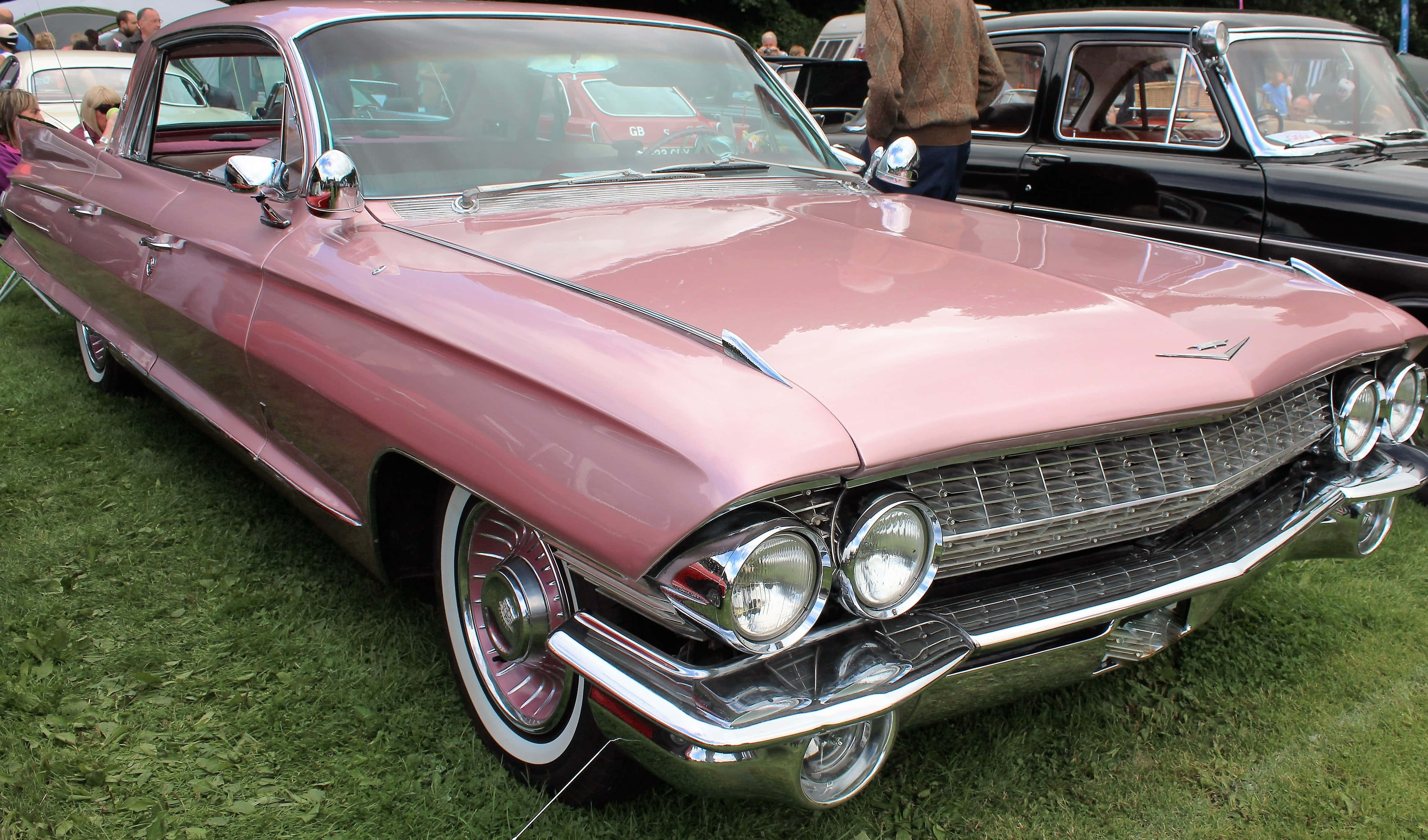 Pink Cadillac 桌布 壁紙 — 一輛閃亮的粉紅色1959年凱迪拉克，帶有鍍鉻裝飾和白邊輪胎，在車展的草地上閃閃發光。