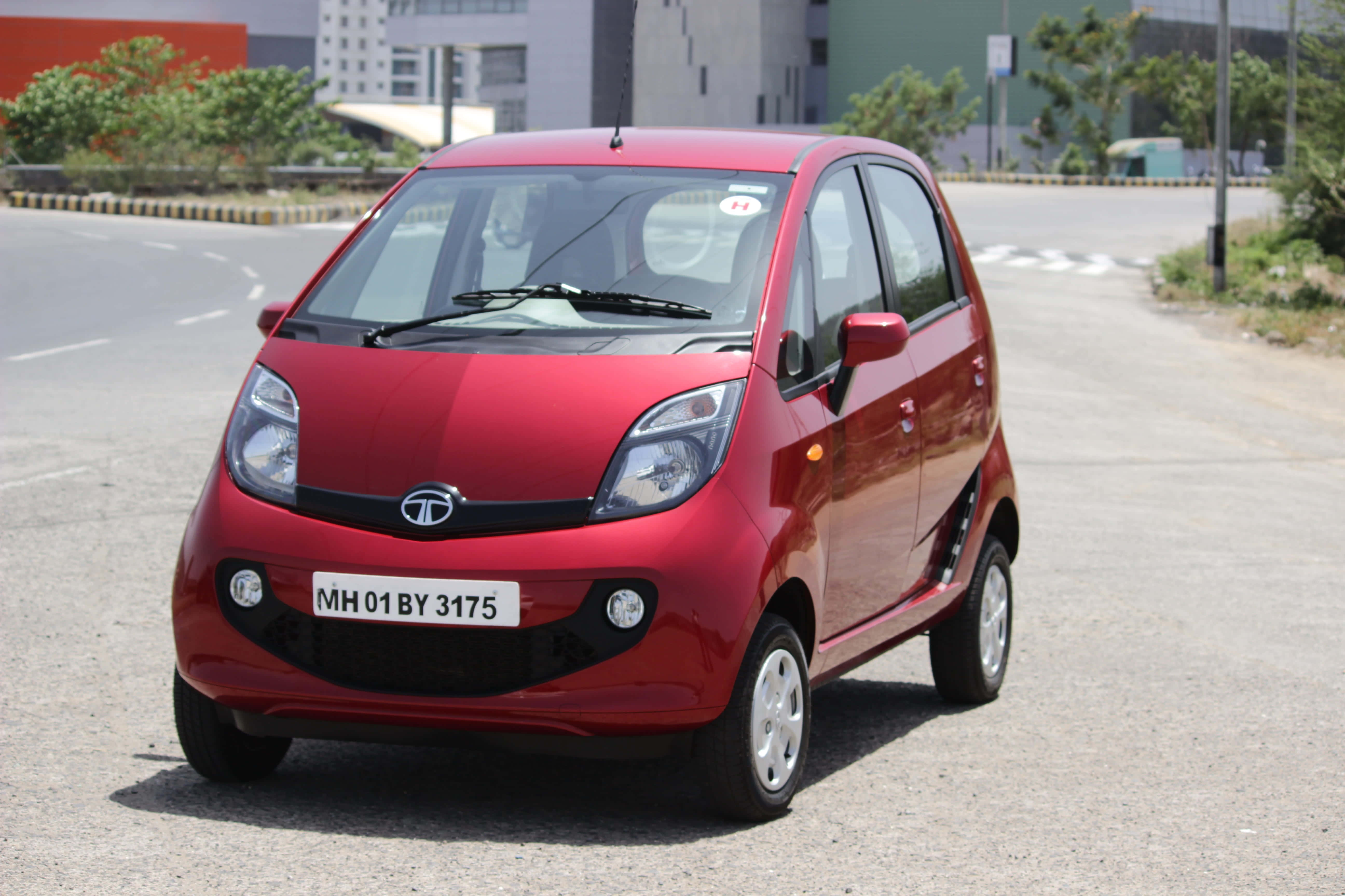 Tata Motors 桌布 壁紙 — 一輛閃亮的紅色 Tata Nano 小型車停在柏油路上，背景有建築物和綠植。