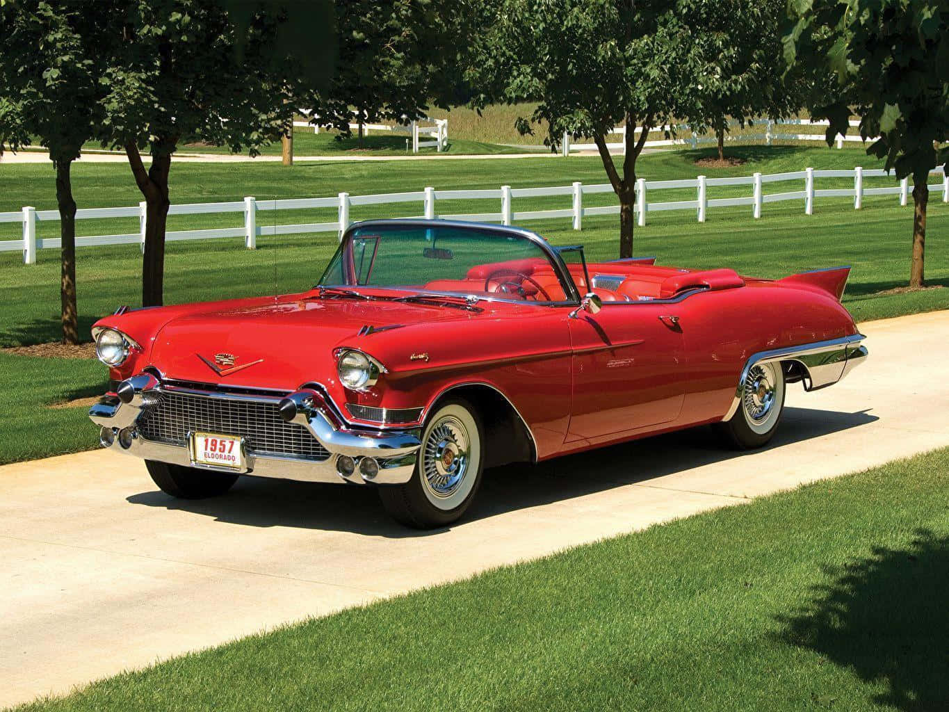 Cadillac 桌布 壁紙 — 一輛閃亮的紅色1957年凱迪拉克敞篷車停在鋪砌的小路上，旁邊是茂密的綠色草地和白色柵欄，在明亮的陽光下。