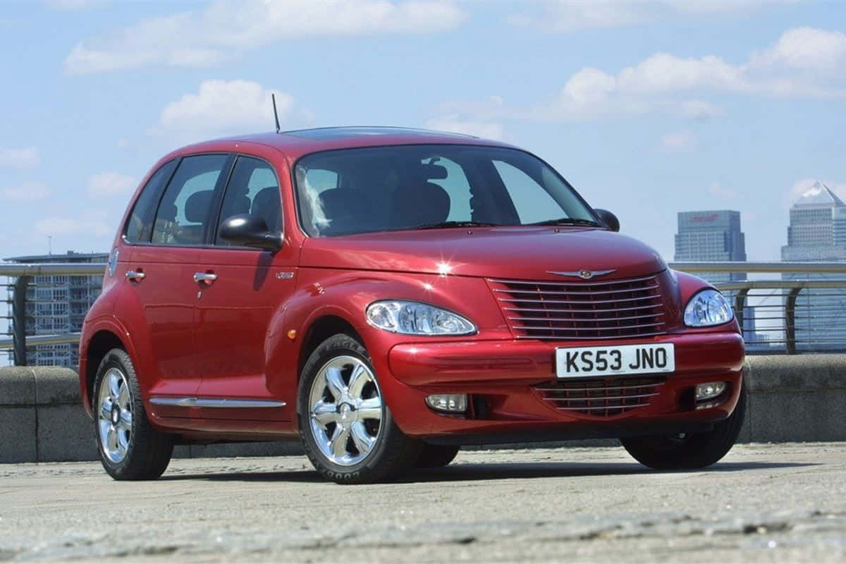 Chrysler Pt Cruiser 桌布 壁紙 — 一輛閃亮的紅色PT Cruiser停泊在混凝土觀景台上，背景是城市天際線和藍天。