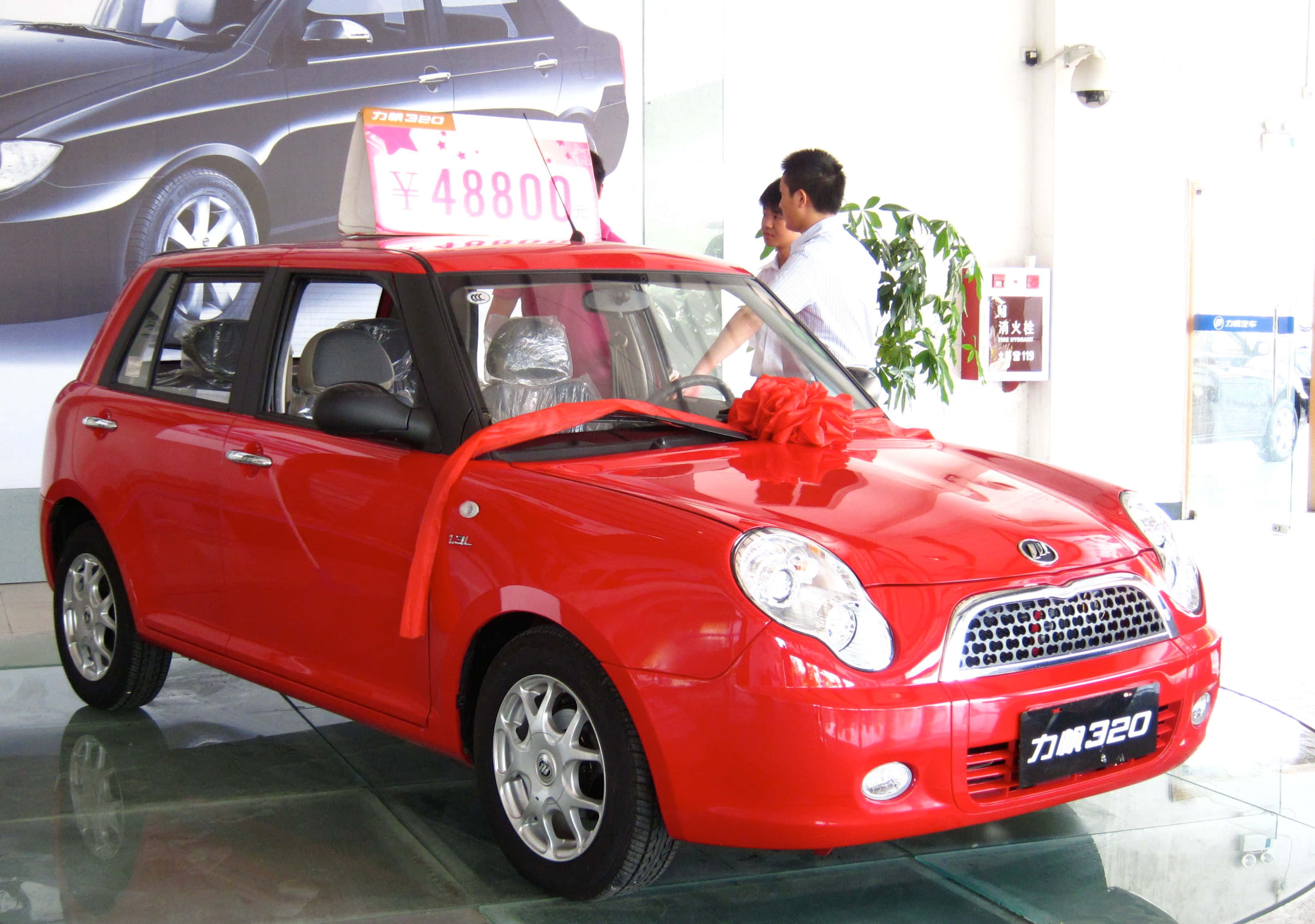 Lifan 桌布 壁紙 — 一輛閃亮的紅色小型汽車，帶有價格標籤和紅色蝴蝶結，展示在明亮的經銷商展廳中。