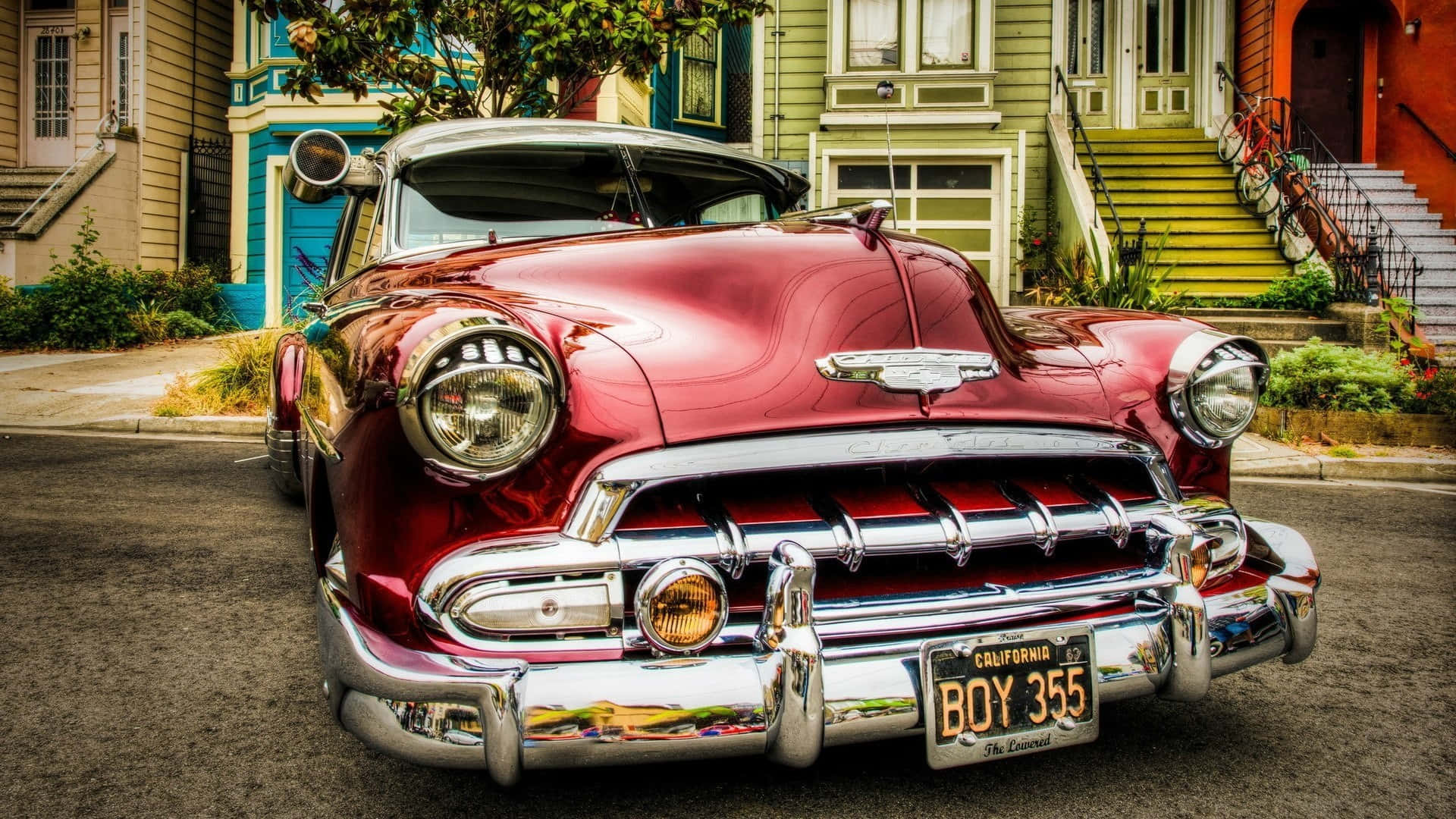 Chevrolet 桌布 壁紙 — 一輛閃亮的紅色經典汽車，帶有鍍鉻細節，停在一條兩旁色彩繽紛的復古房屋的街道上。