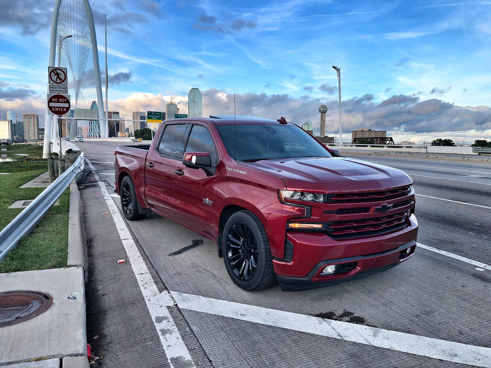 Trucks 桌布 壁紙 — 一輛閃亮的紅色雪佛蘭Silverado皮卡車停放在都市高速公路上，背景有現代橋樑和城市天際線，天空局部多雲。