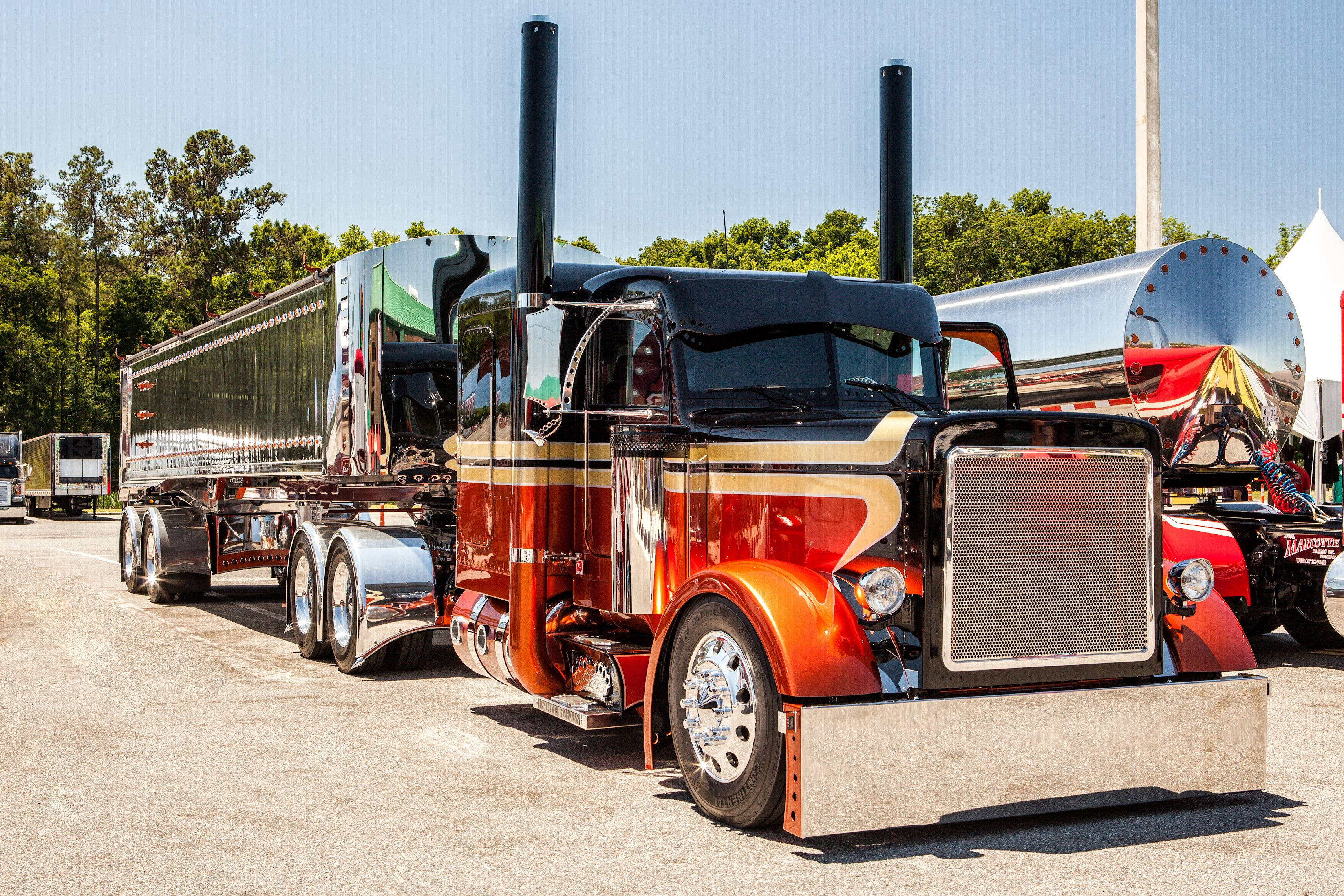 Kenworth W900 桌布 壁紙 — 一輛閃亮的紅黑色經典半掛卡車，帶有鍍鉻裝飾和雙排氣管，停在陽光明媚的戶外場地。