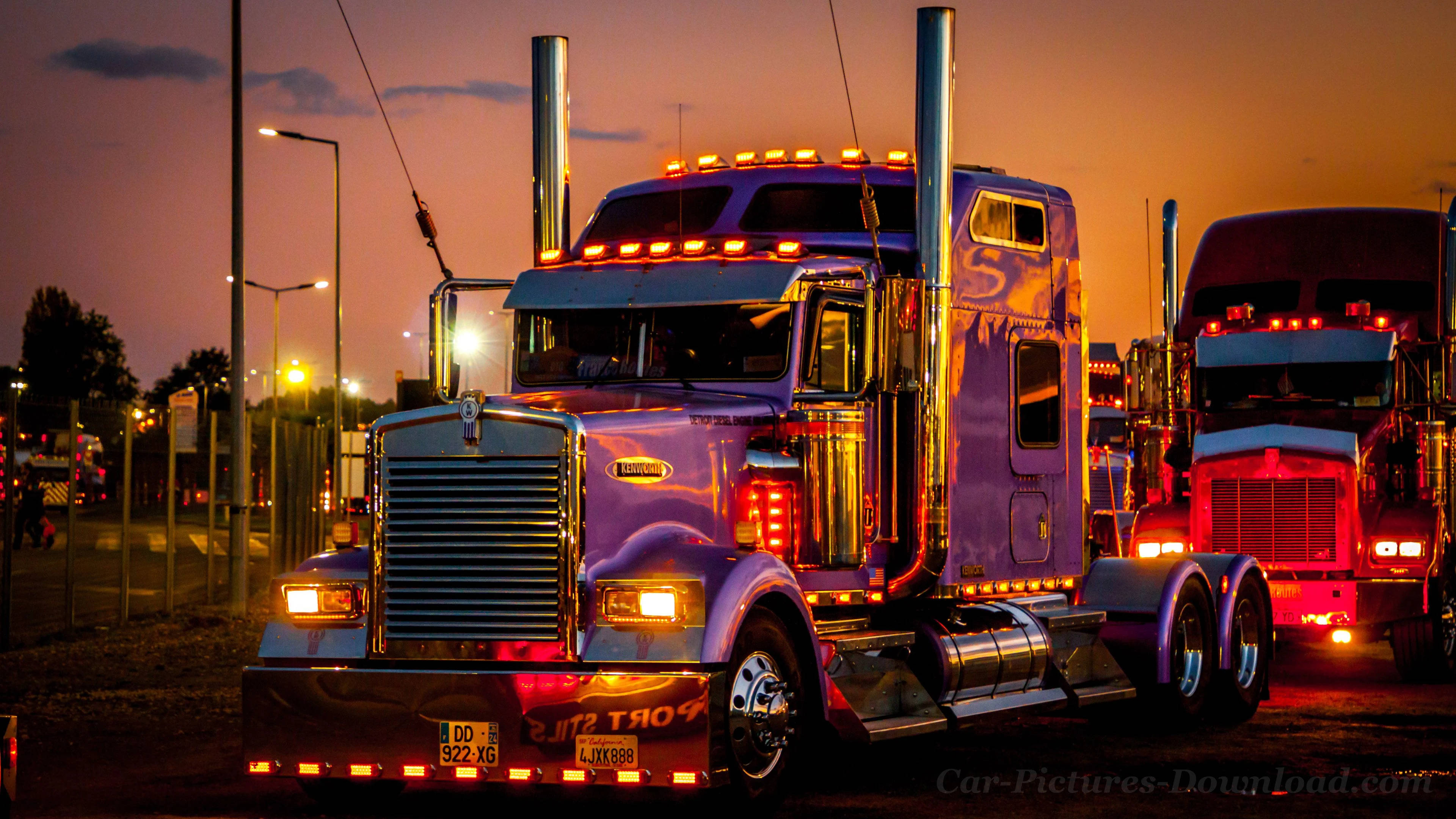 Trucks 桌布 壁紙 — 一輛閃亮的紫色半掛卡車，帶有鍍鉻裝飾和發光的琥珀色燈光，在黃昏時停泊，反射著溫暖的橙色天空。