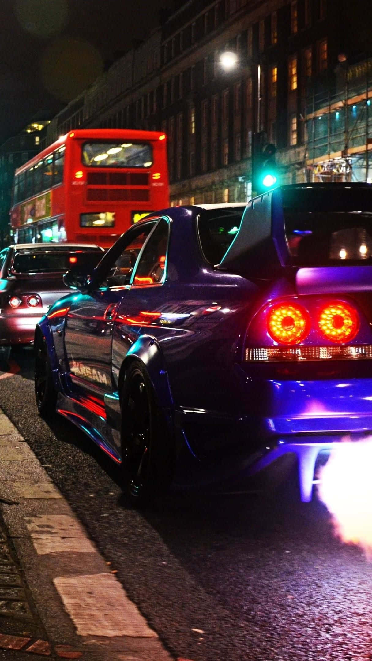 R33 GT-R 桌布 壁紙 — 一輛閃亮的紫色跑車，帶有發光的橙色尾燈和藍色底盤燈，在夜間濕漉漉的城市街道上行駛，背景中有一輛紅色的雙層巴士。
