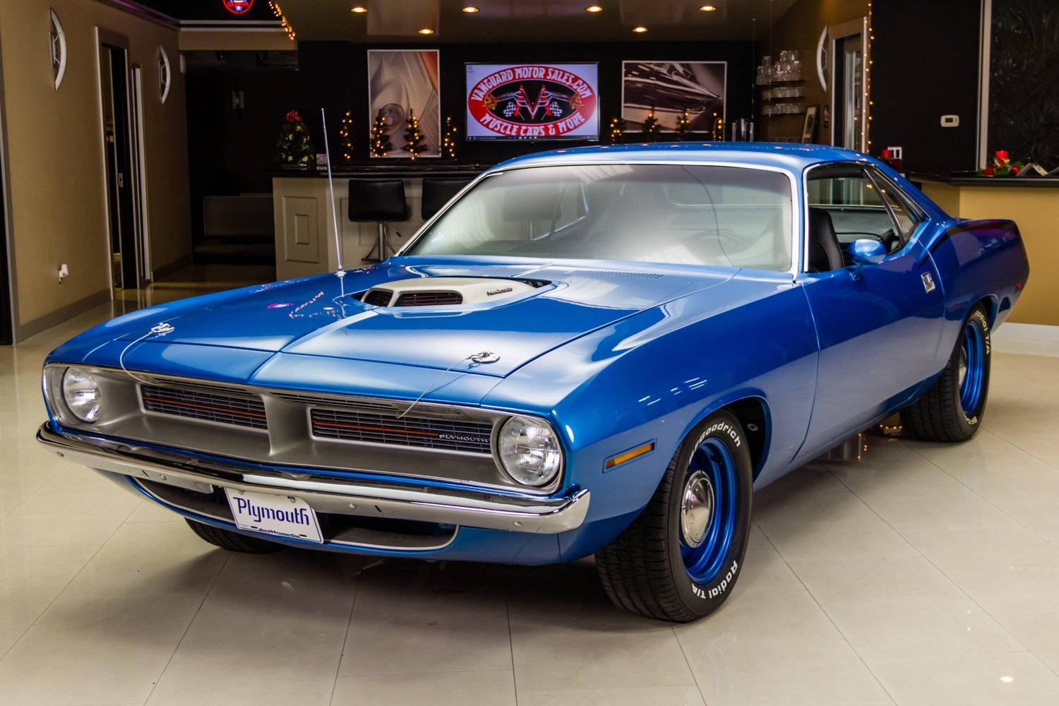Barracuda 桌布 壁紙 — 一輛閃亮的藍色1970年代Plymouth肌肉車在展廳燈光下閃耀，配備鍍鉻裝飾和定制輪圈。