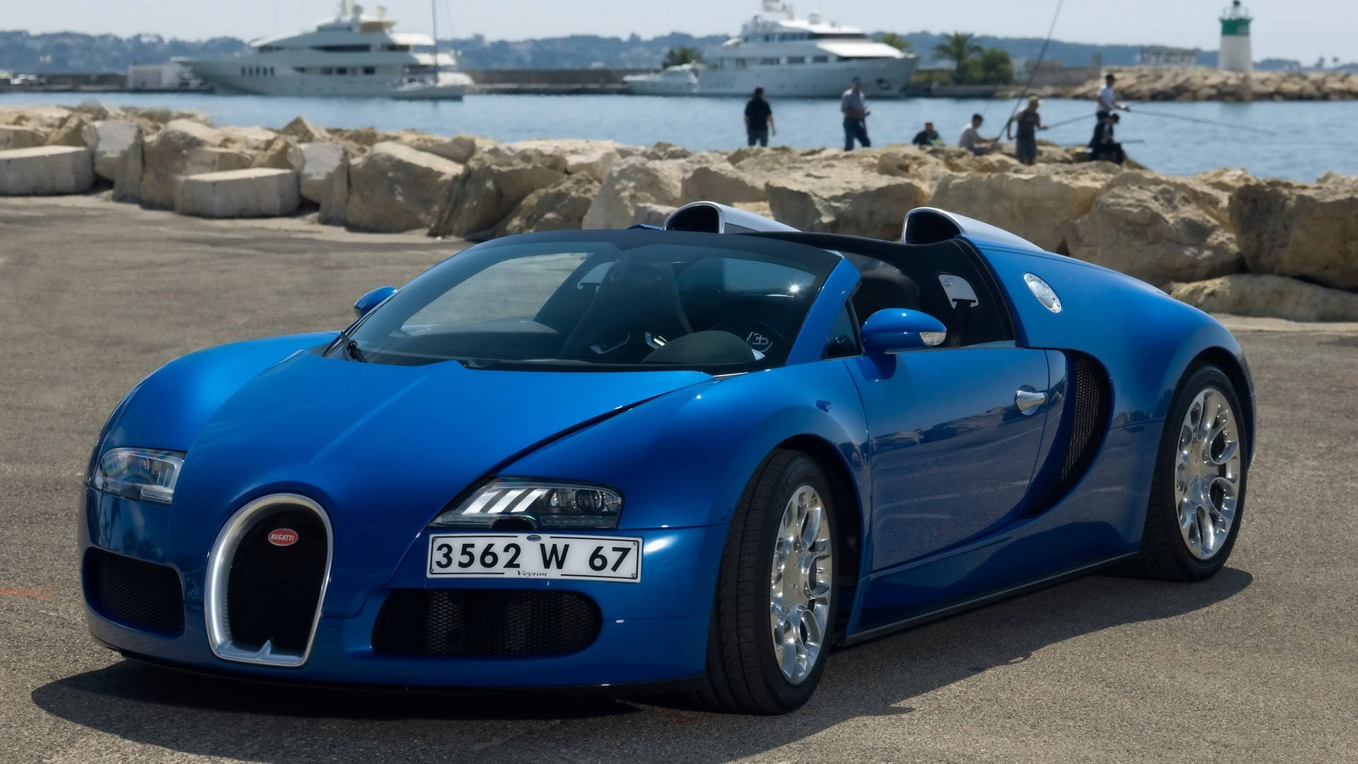 bugatti iPhone 桌布 壁紙 — 一輛閃亮的藍色Bugatti Veyron超級跑車停泊在陽光明媚的港口碼頭，背景有遊艇和人。