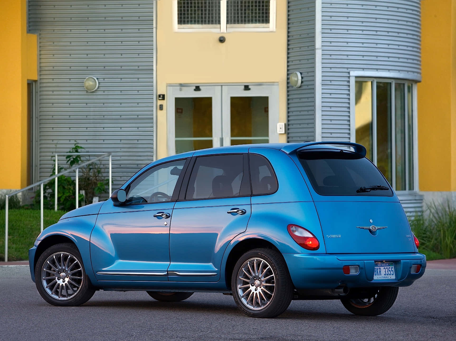 Chrysler Pt Cruiser 桌布 壁紙 — 一輛閃亮的藍色PT Cruiser停放在現代建築前的柏油路上，建築物有黃色和灰色的牆壁。