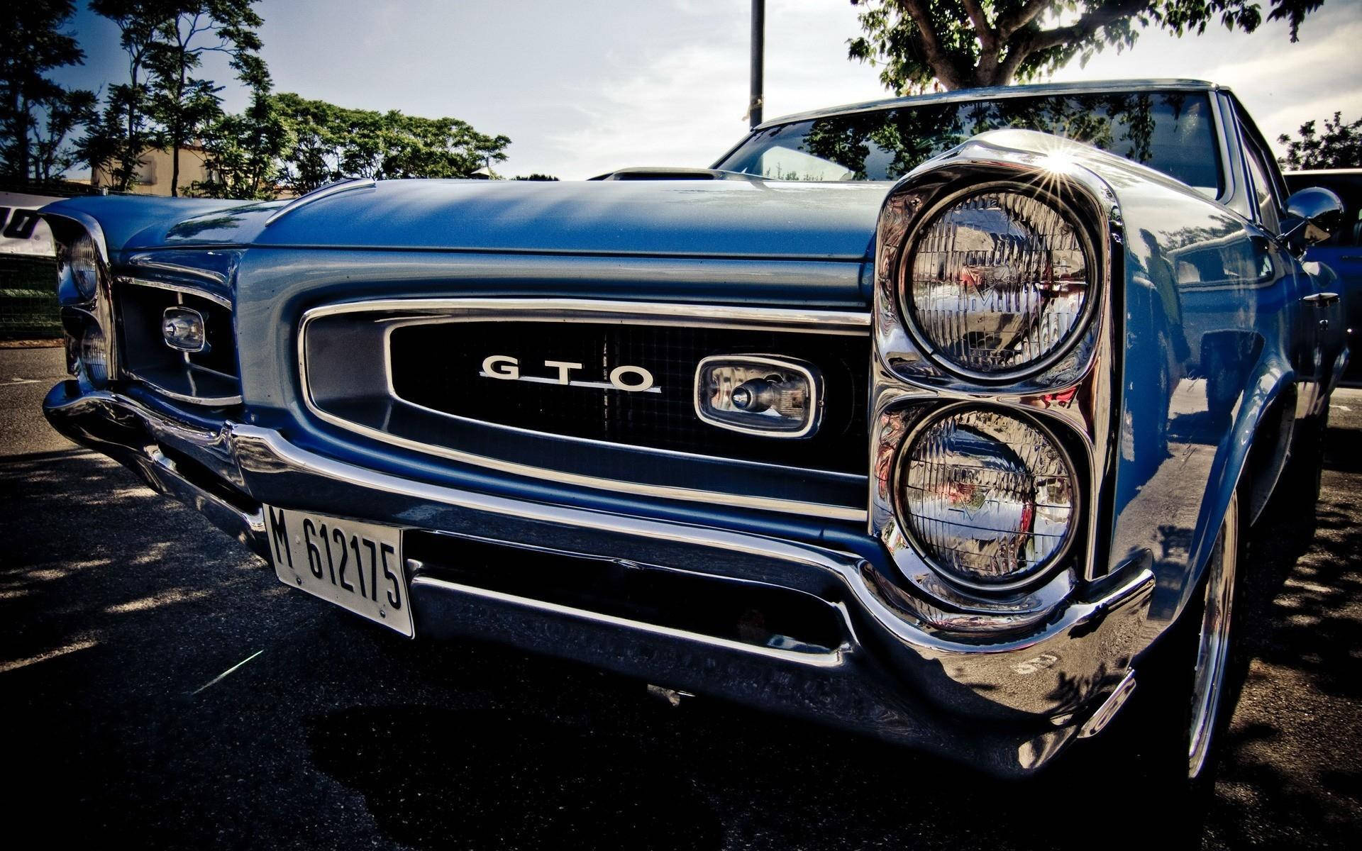Pontiac 桌布 壁紙 — 一輛閃亮的藍色經典 GTO 肌肉車，帶有鍍鉻細節和圓形頭燈，停在明亮的日光下。