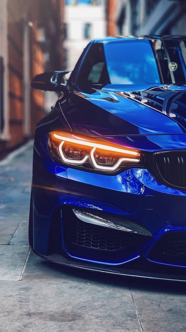BMW 動圖 桌布 壁紙 — 一輛閃亮的藍色跑車，帶有發光的車頭燈，停在一條狹窄的城市街道上。