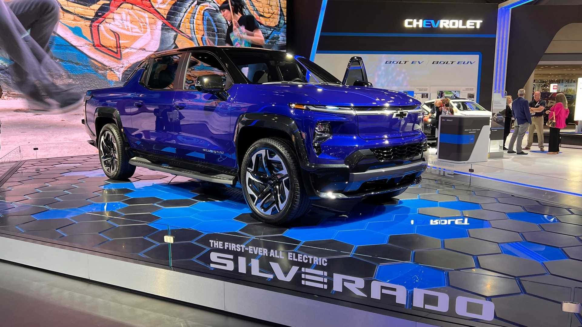 Chevrolet 桌布 壁紙 — 一輛閃亮的藍色雪佛蘭Silverado EV卡車，在六邊形藍黑舞台上展示，背景有人群。