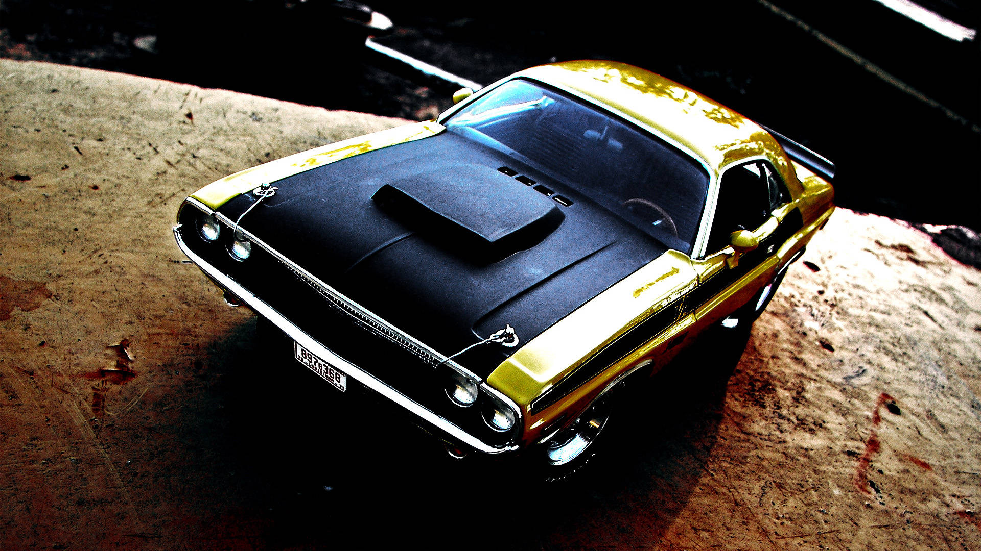 Challenger 桌布 壁紙 — 一輛閃亮的金色和黑色經典肌肉車，帶有引擎蓋進氣口，在高對比度照明下戲劇性地停在風化的混凝土表面上。