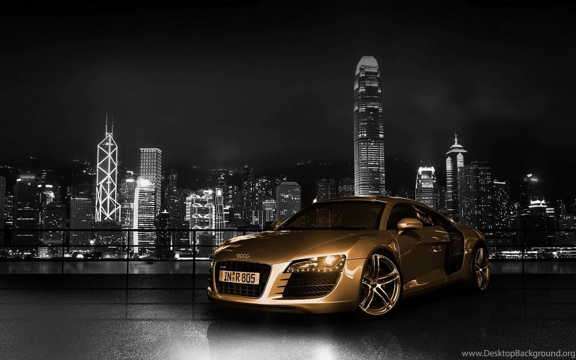 高清 桌布 壁紙 — 一輛閃亮的金色奧迪R8跑車在夜間停放，背後是單色的香港天際線。
