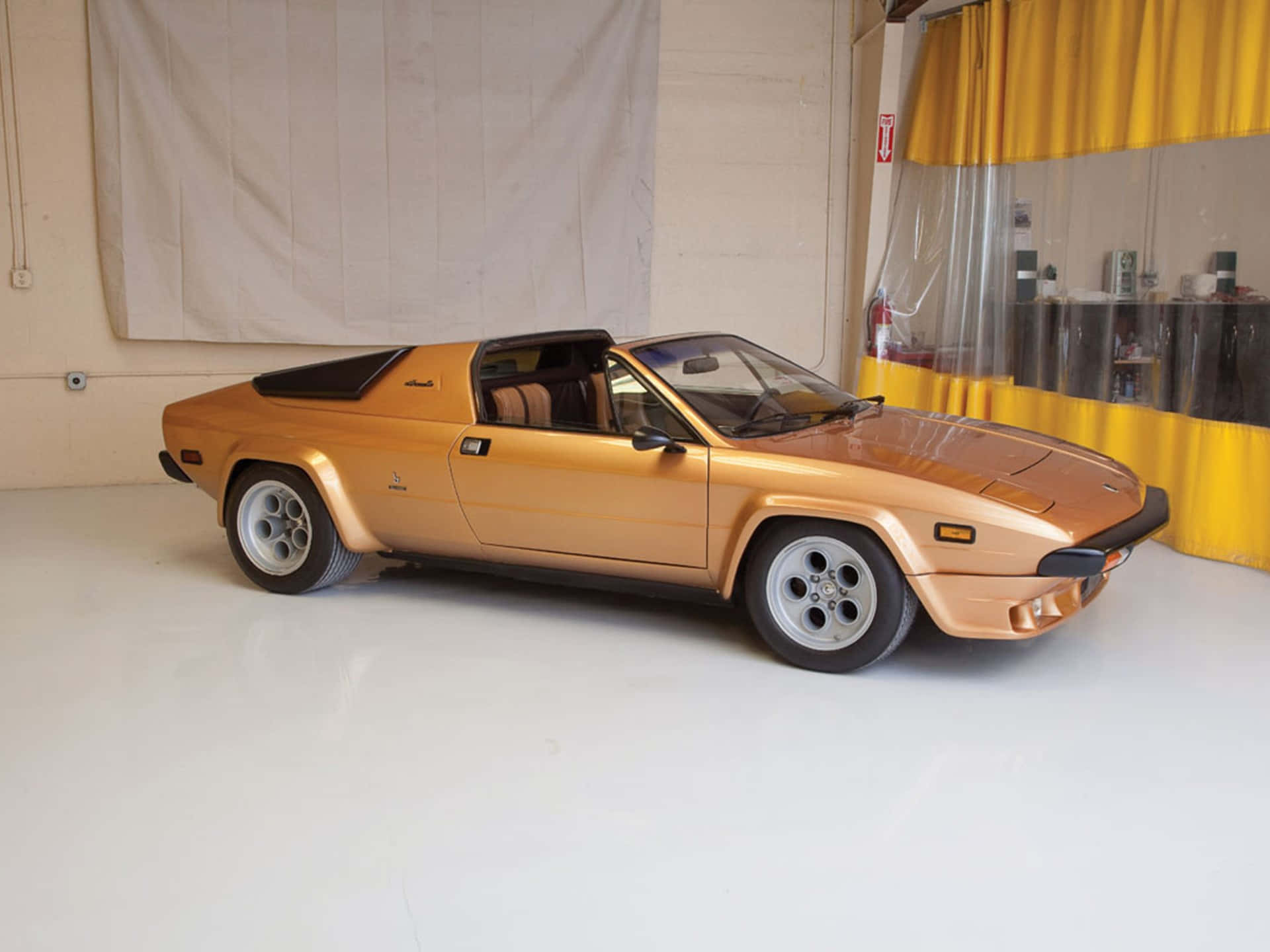 Lamborghini Silhouette 桌布 壁紙 — 一輛閃亮的金色復古跑車帶有黑色點綴，停放在一個乾淨的白色車庫內，背景有黃色窗簾。