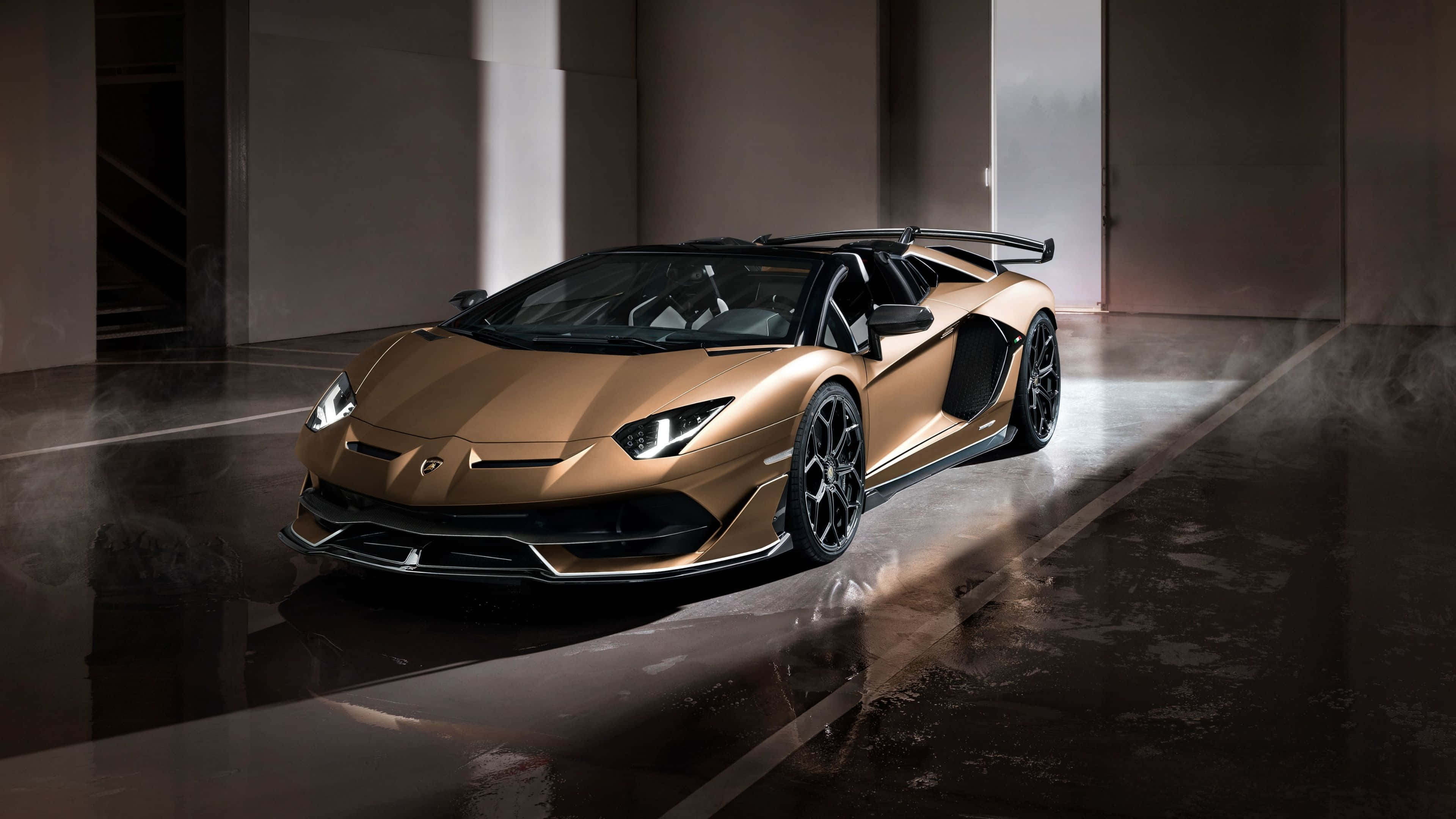 4K 藍寶堅尼 桌布 壁紙 — 一輛閃亮的金色藍寶堅尼 Aventador SVJ Roadster 停放在燈光昏暗的工業車庫中，帶有戲劇性的聚光燈效果。