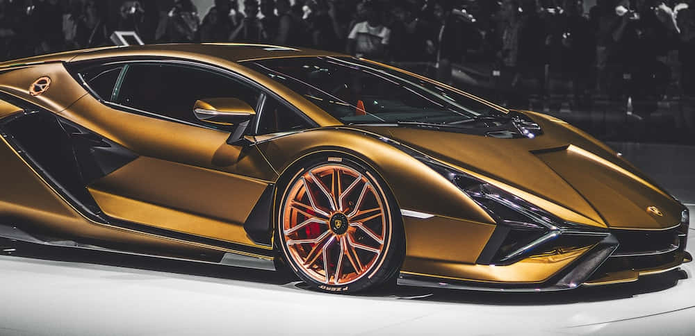 Cool Lamborghinis 桌布 壁紙 — 一輛閃亮的金色藍寶堅尼跑車配銅色輪圈在車展上展出，背景有模糊的觀眾。