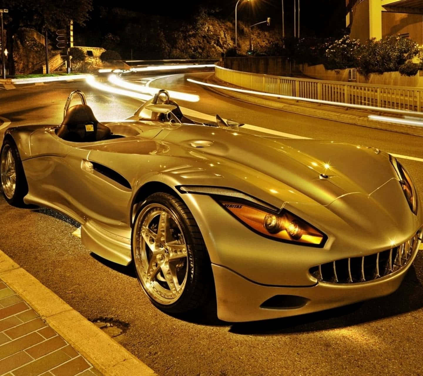 Gold Cars 桌布 壁紙 — 一輛閃亮的金色跑車在夜間停泊，濕滑路面上有來往車輛的光軌。