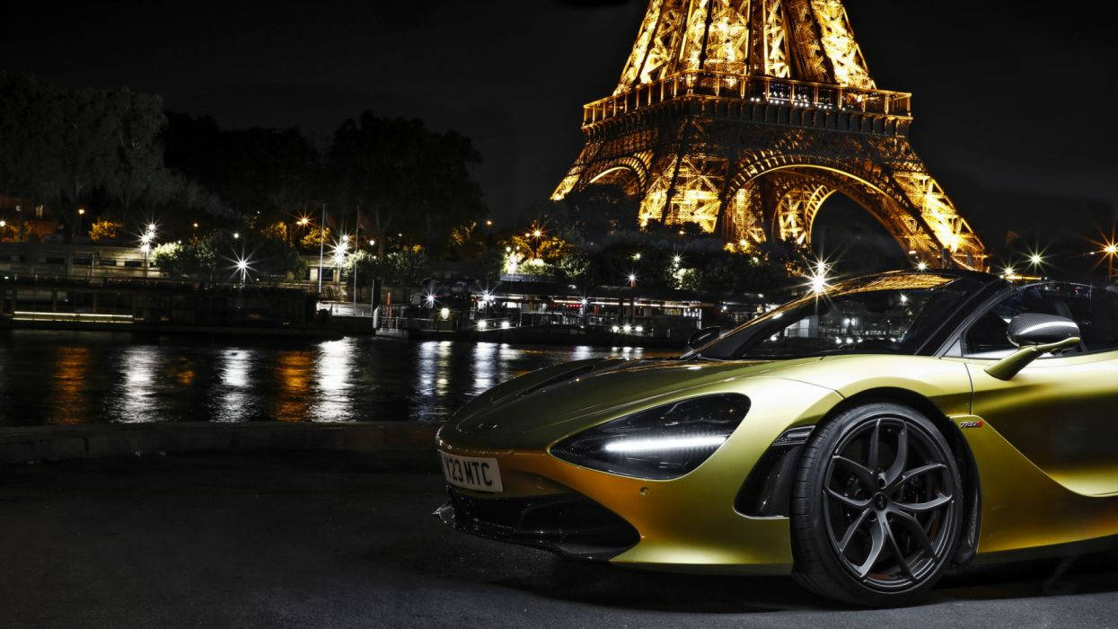 Eiffel Tower 桌布 壁紙 — 一輛閃亮的金色跑車在夜間停泊，背後亮燈的艾菲爾鐵塔倒映在塞納河中。
