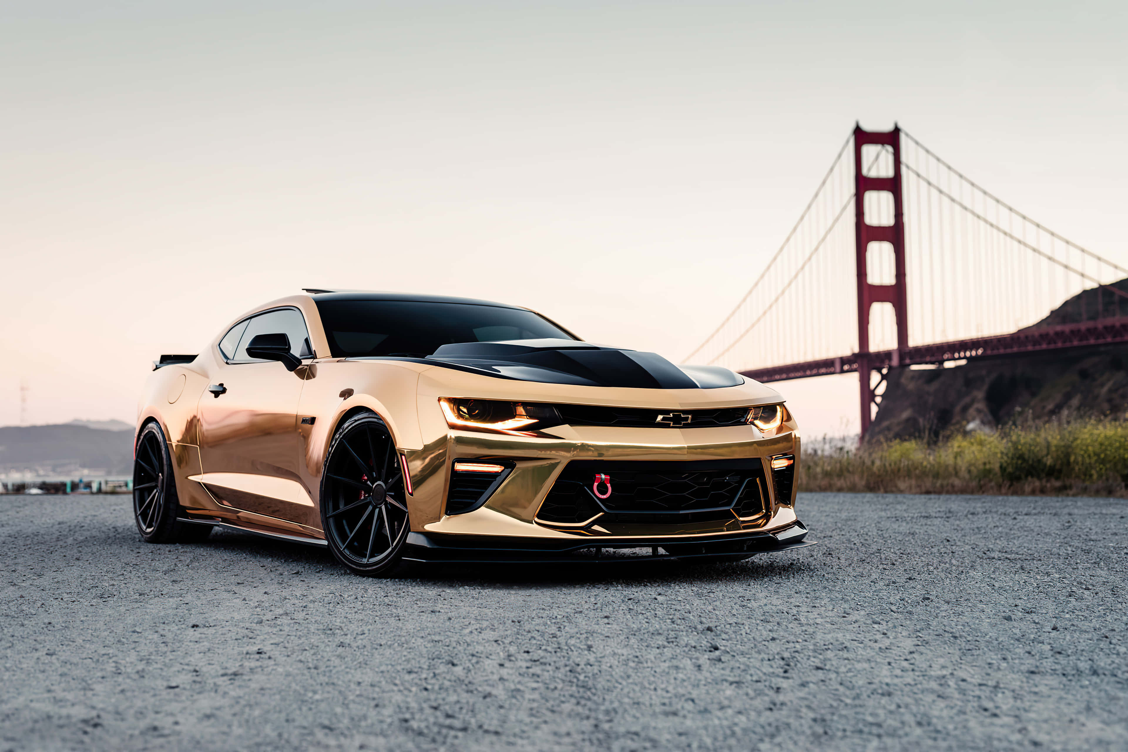 Gold Cars 桌布 壁紙 — 一輛閃亮的金色雪佛蘭Camaro，帶有黑色點綴，在黃昏時停泊在柏油路上，背景是金門大橋。
