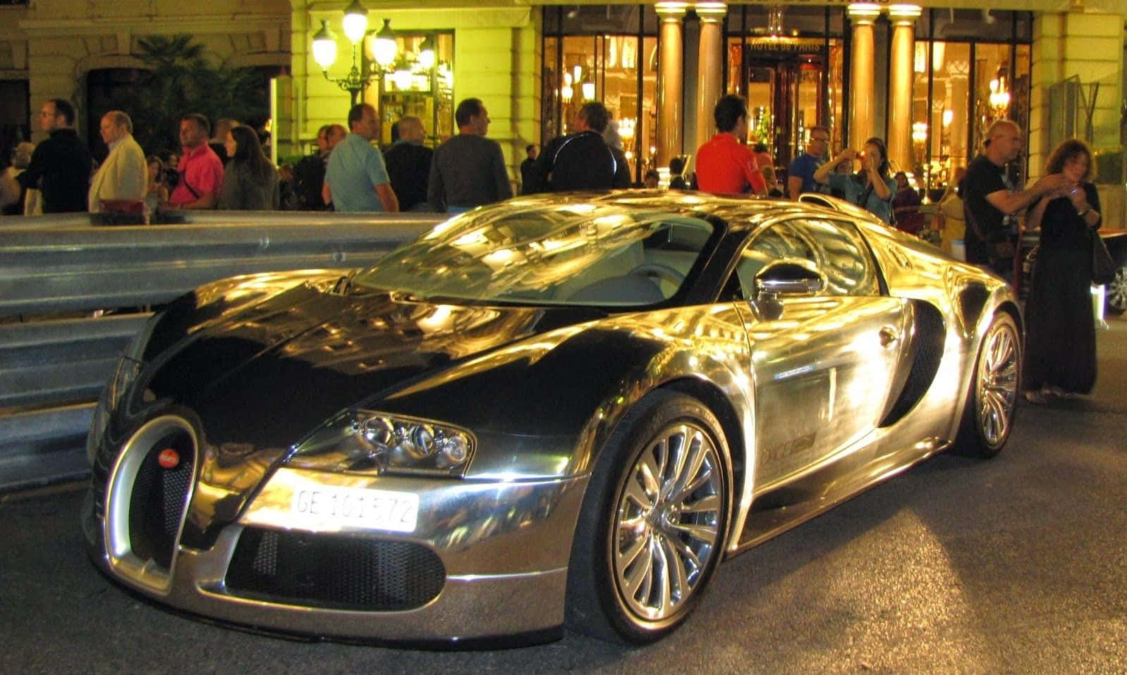 人物 桌布 壁紙 — 一輛閃亮的銀色Bugatti Veyron在夜間停車，人們聚集在護欄後方，身處燈光明亮的城市環境中。