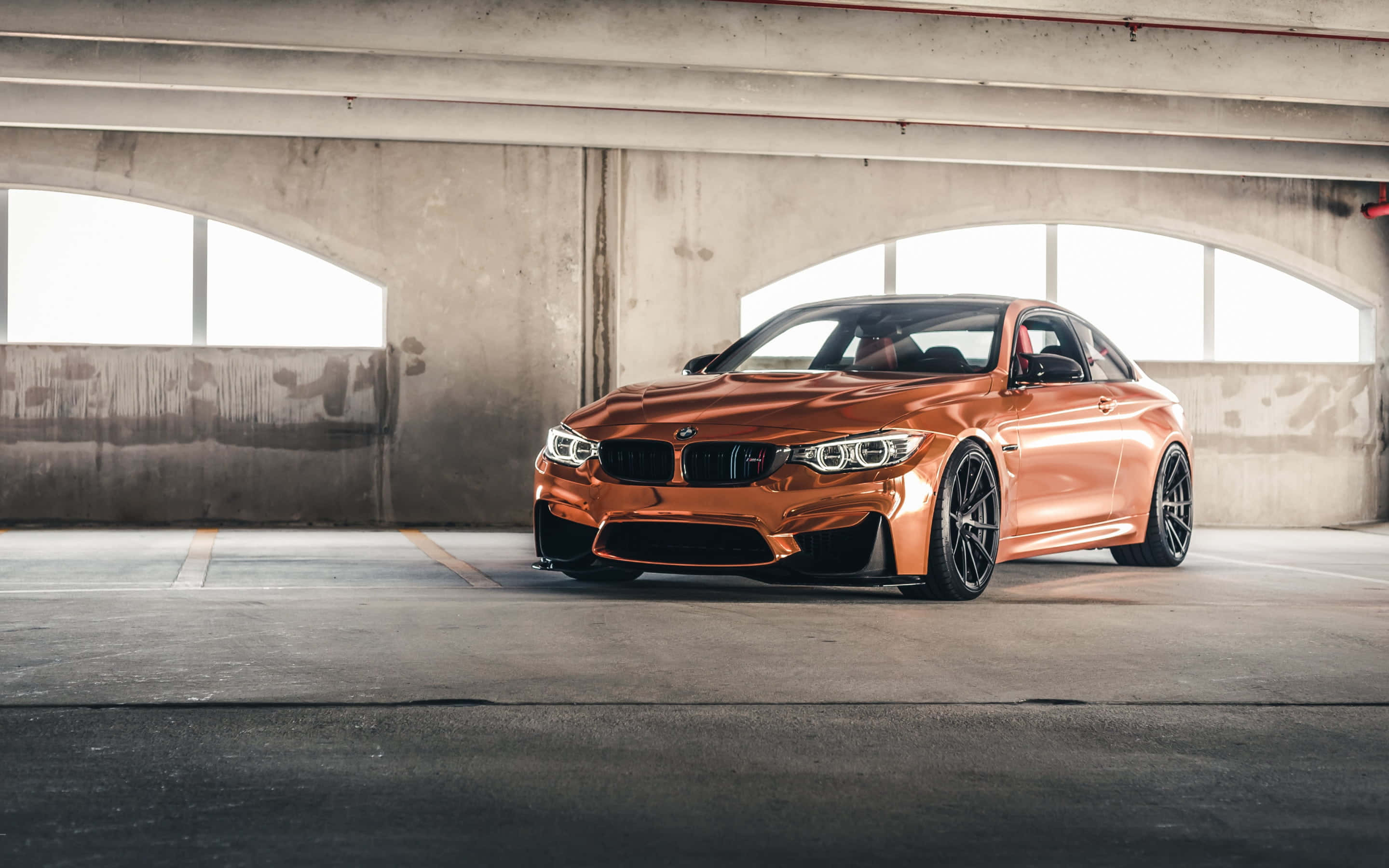 Bronze 桌布 壁紙 — 一輛閃亮的銅色BMW M4雙門跑車停放在帶拱形窗的混凝土停車場下。