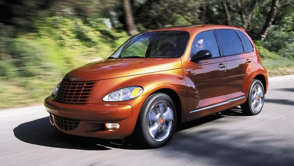 Chrysler Pt Cruiser 桌布 壁紙 — 一輛閃亮的銅色PT Cruiser在綠樹成蔭的道路上行駛，背景帶有動態模糊效果。