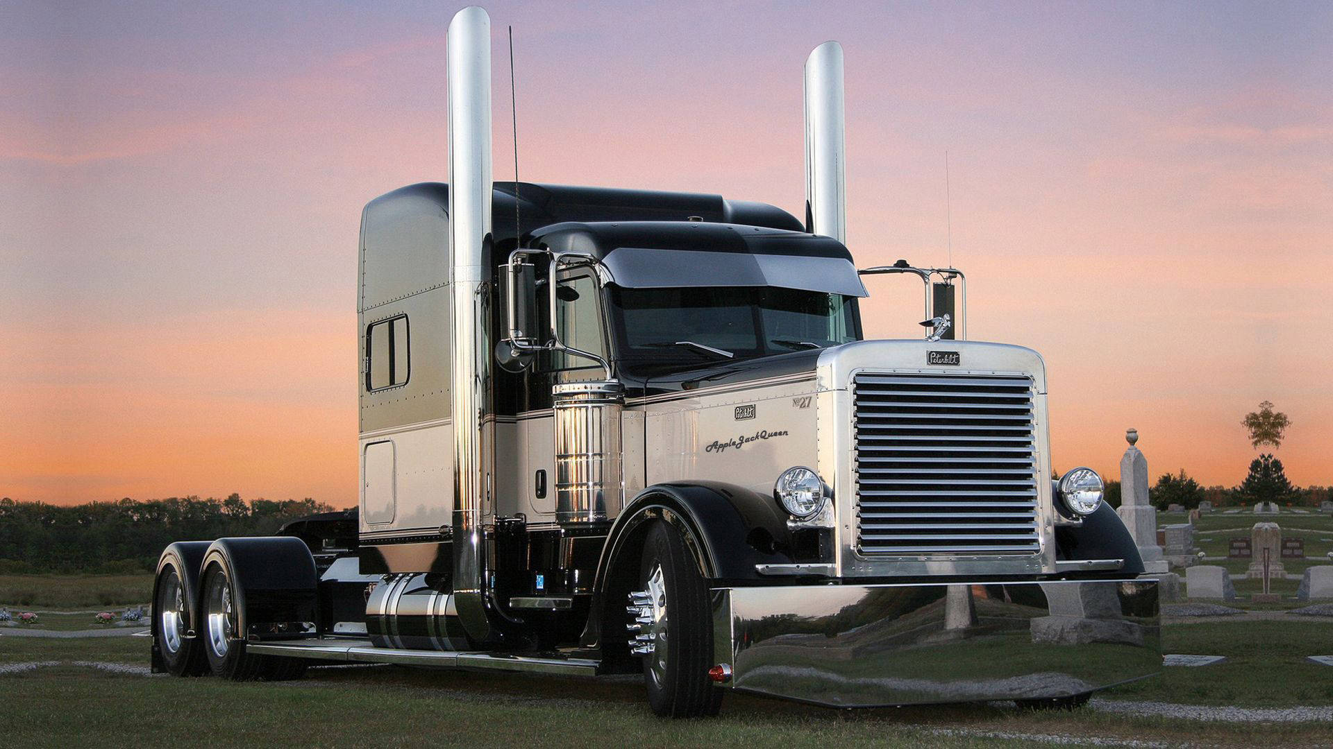 Peterbilt 桌布 壁紙 — 一輛閃亮的鍍鉻半掛卡車在日落時分自豪地矗立在墓地中，天空呈現粉紅色和橙色。