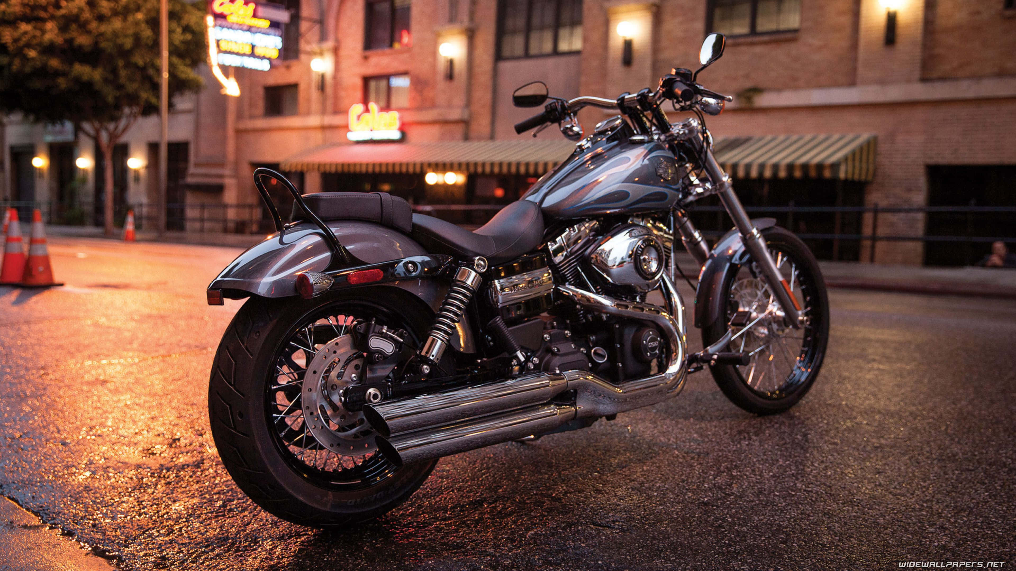 Harley Davidson HD 桌布 壁紙 — 一輛閃亮的鍍鉻機車在夜間停泊在濕漉漉的城市街道上，被溫暖的霓虹燈招牌和街燈照亮。