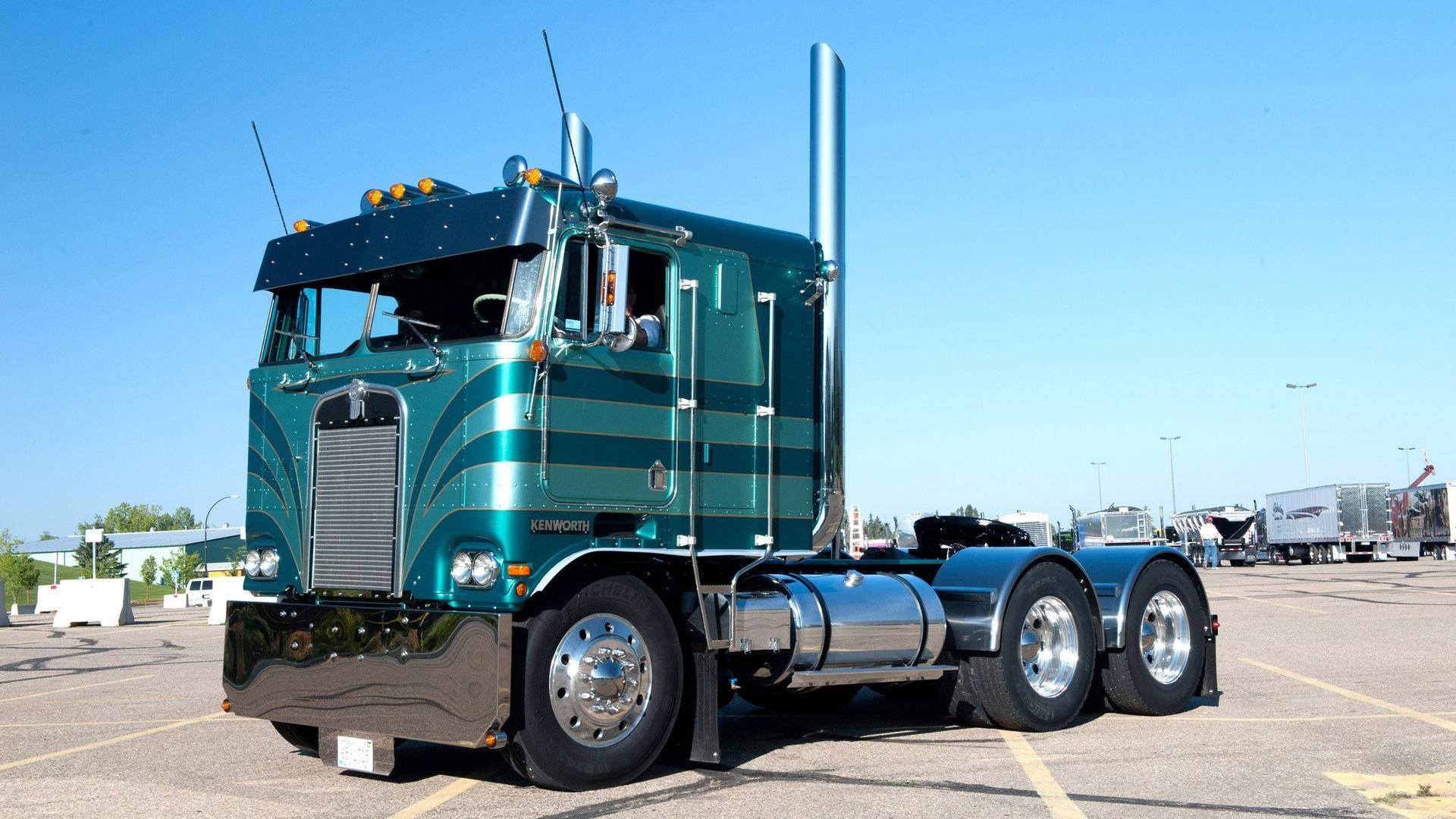 Kenworth 桌布 壁紙 — 一輛閃亮的青綠色Kenworth半掛卡車，帶有鍍鉻裝飾，停在晴朗藍天下的陽光充足地段。