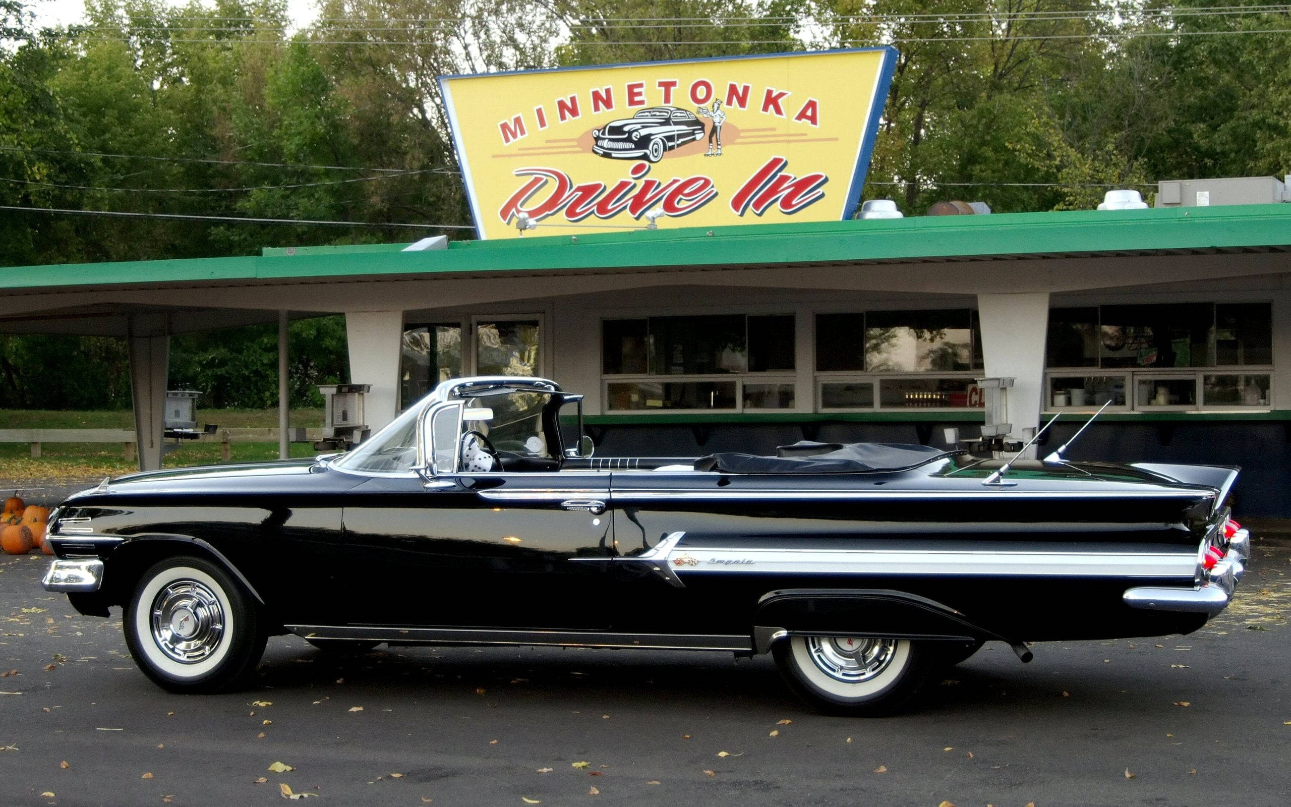 高清 桌布 壁紙 — 一輛閃亮的黑色1950年代敞篷車停在復古的Minnetonka Drive In前，地上散落著秋天的落葉。