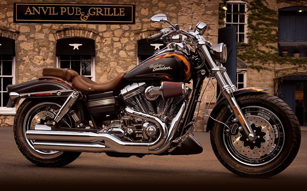 Harley 桌布 壁紙 — 一輛閃亮的黑色Harley-Davidson機車，帶有鍍鉻裝飾，停在寫有「Anvil Pub & Grille」的質樸石建築前。