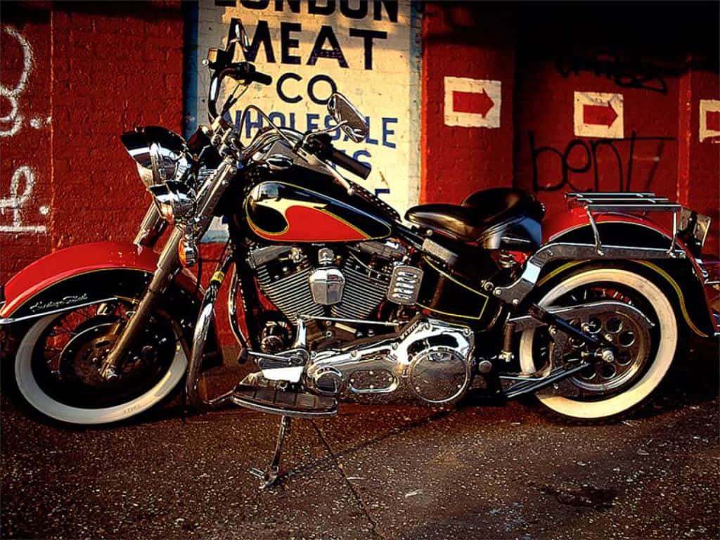 Harley Davidson HD 桌布 壁紙 — 一輛閃亮的黑色和紅色訂製摩托車，帶有鍍鉻裝飾，在溫暖的燈光下停在一幅塗鴉覆蓋的紅磚牆前。