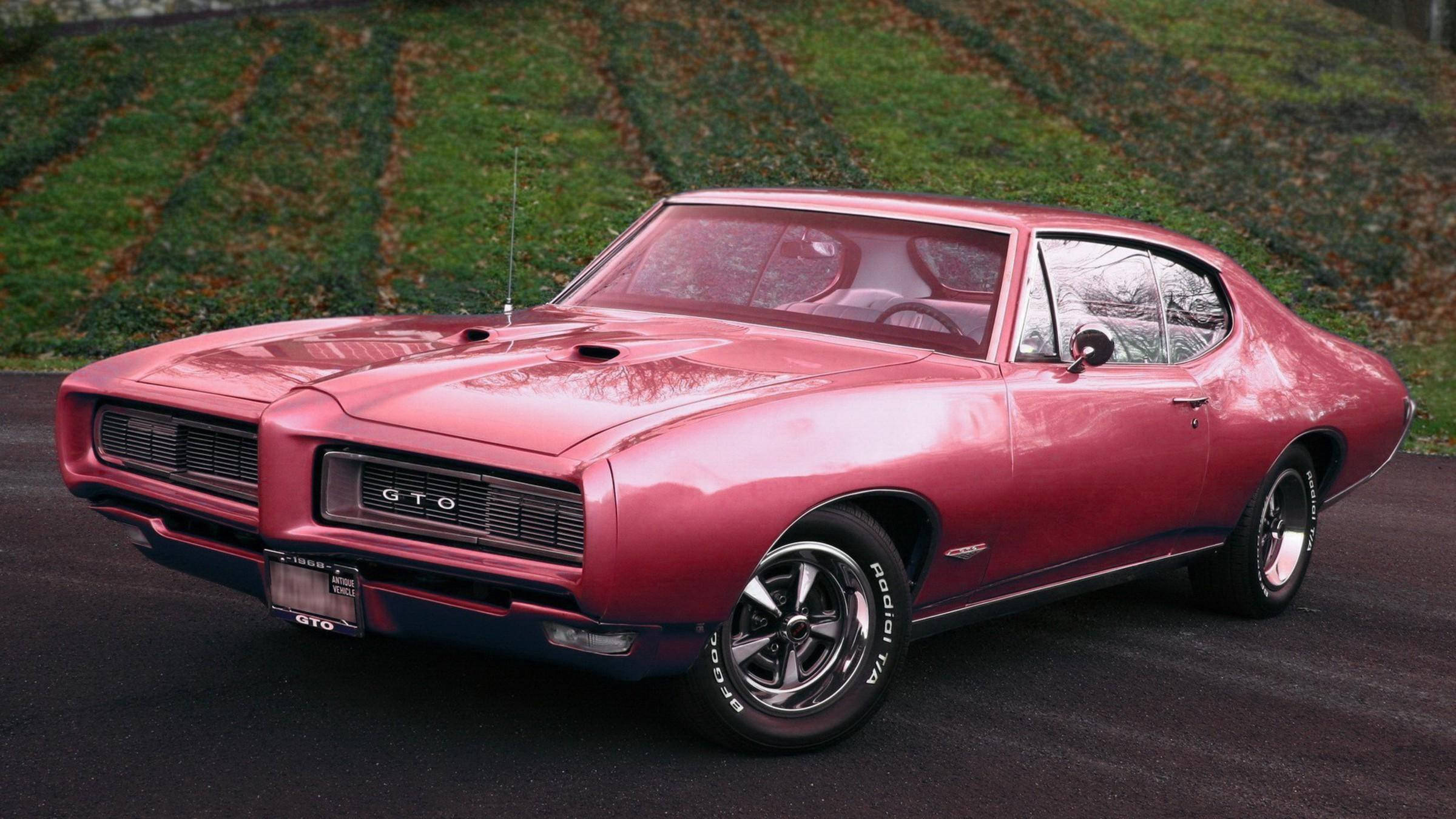 龐蒂克 桌布 壁紙 — 一輛閃亮粉紅色1960年代Pontiac GTO肌肉車停在瀝青路上，背景有草地山坡。