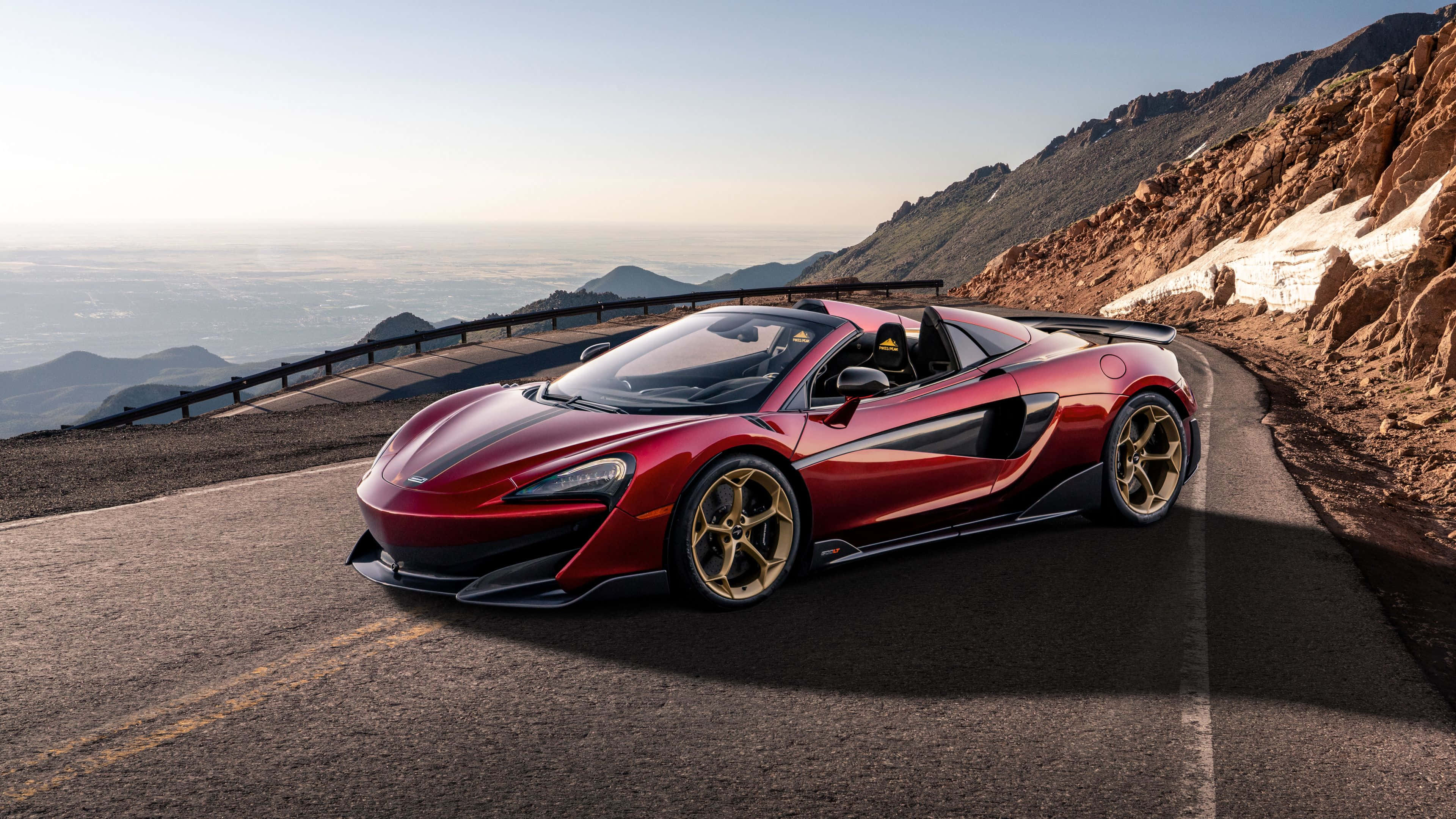 Mclaren 600lt 桌布 壁紙 — 一輛閃亮紅色McLaren跑車搭配金色輪圈，在日出時沿著蜿蜒山路行駛，俯瞰廣闊山谷。