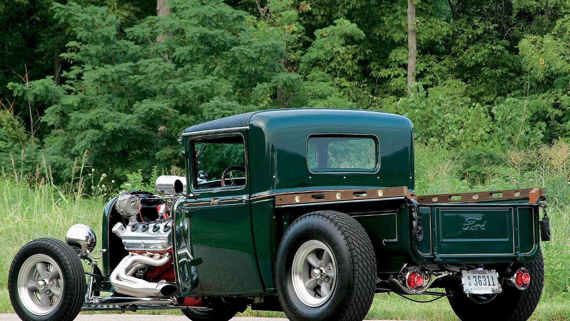 old 桌布 壁紙 — 一輛閃亮綠色復古福特 hot rod 卡車，帶有外露鍍鉻引擎和訂製輪圈，停泊在茂密綠樹旁的草地上。