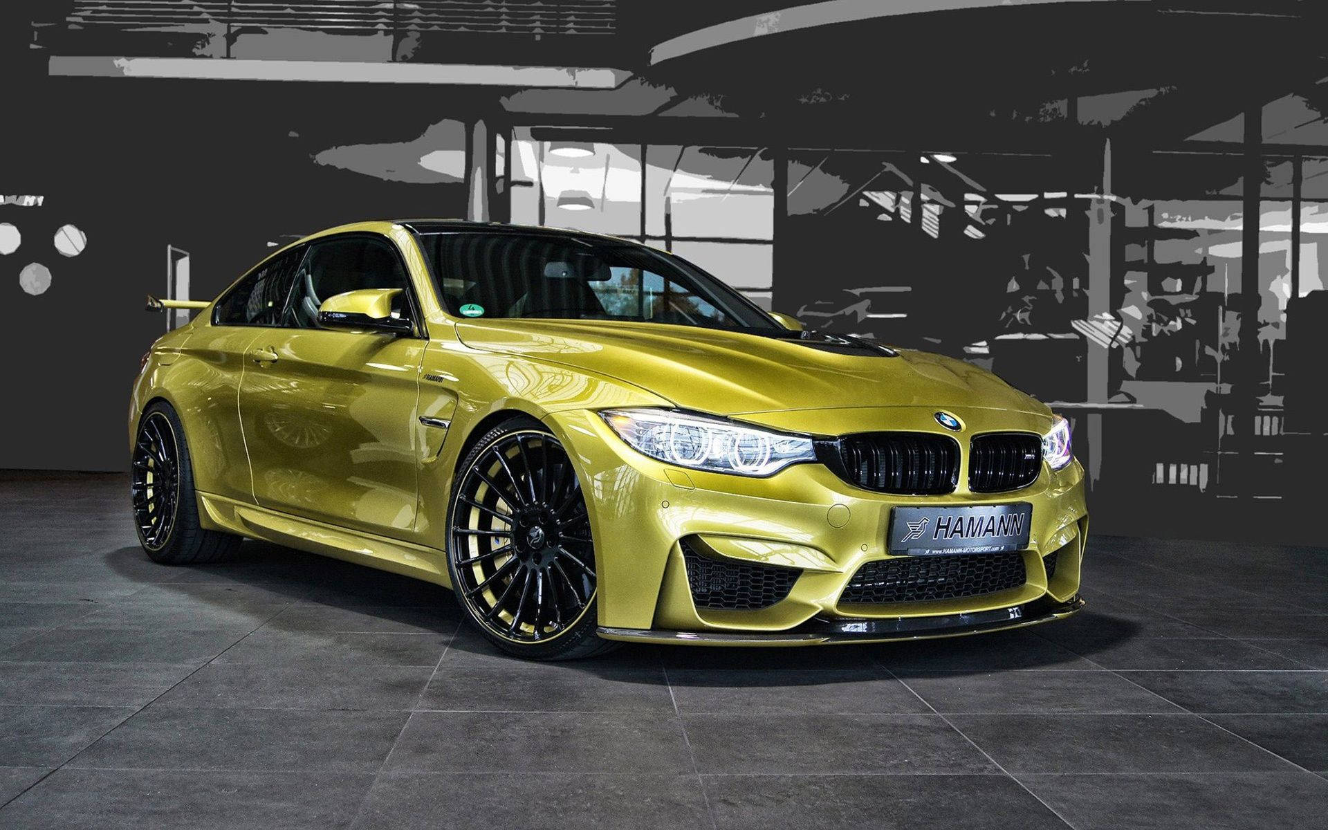 m 桌布 壁紙 — 一輛閃耀金色的Hamann改裝BMW M4轎跑車，在簡約工業風車庫中展示，背景為單色調。