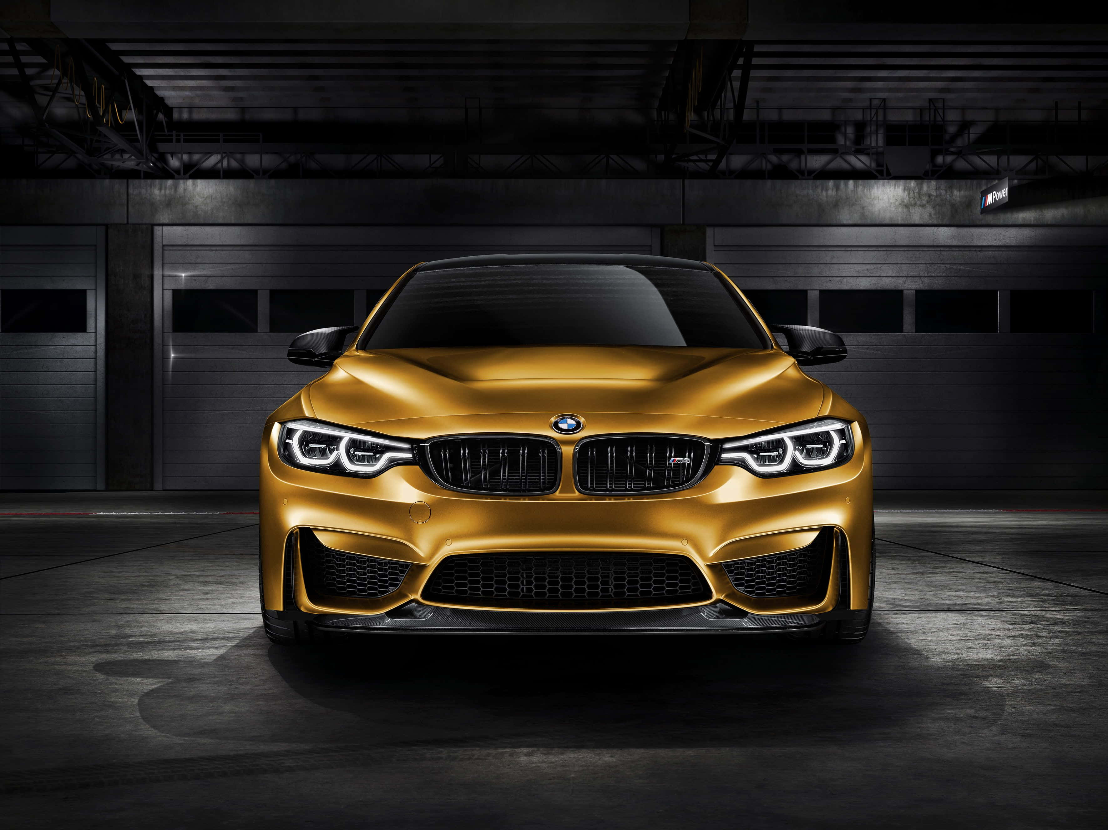 Gold Cars 桌布 壁紙 — 一輛閃閃發光的金色BMW M4跑車在一個黑暗的工業車庫中戲劇性地被照亮，車庫有裸露的橫樑和混凝土地板。