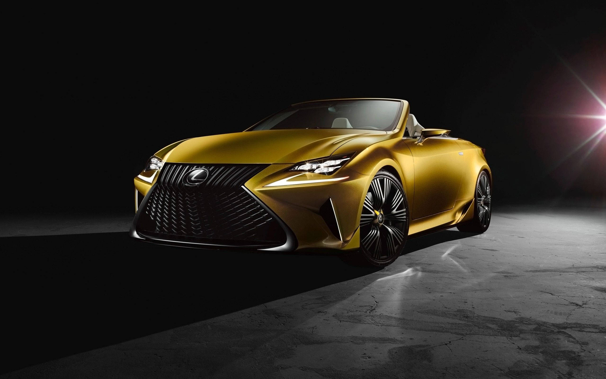 Lexus 標誌 桌布 壁紙 — 一輛閃閃發光的金色Lexus敞篷跑車在黑暗的攝影棚背景下，以明亮的鏡頭光暈戲劇性地照亮。